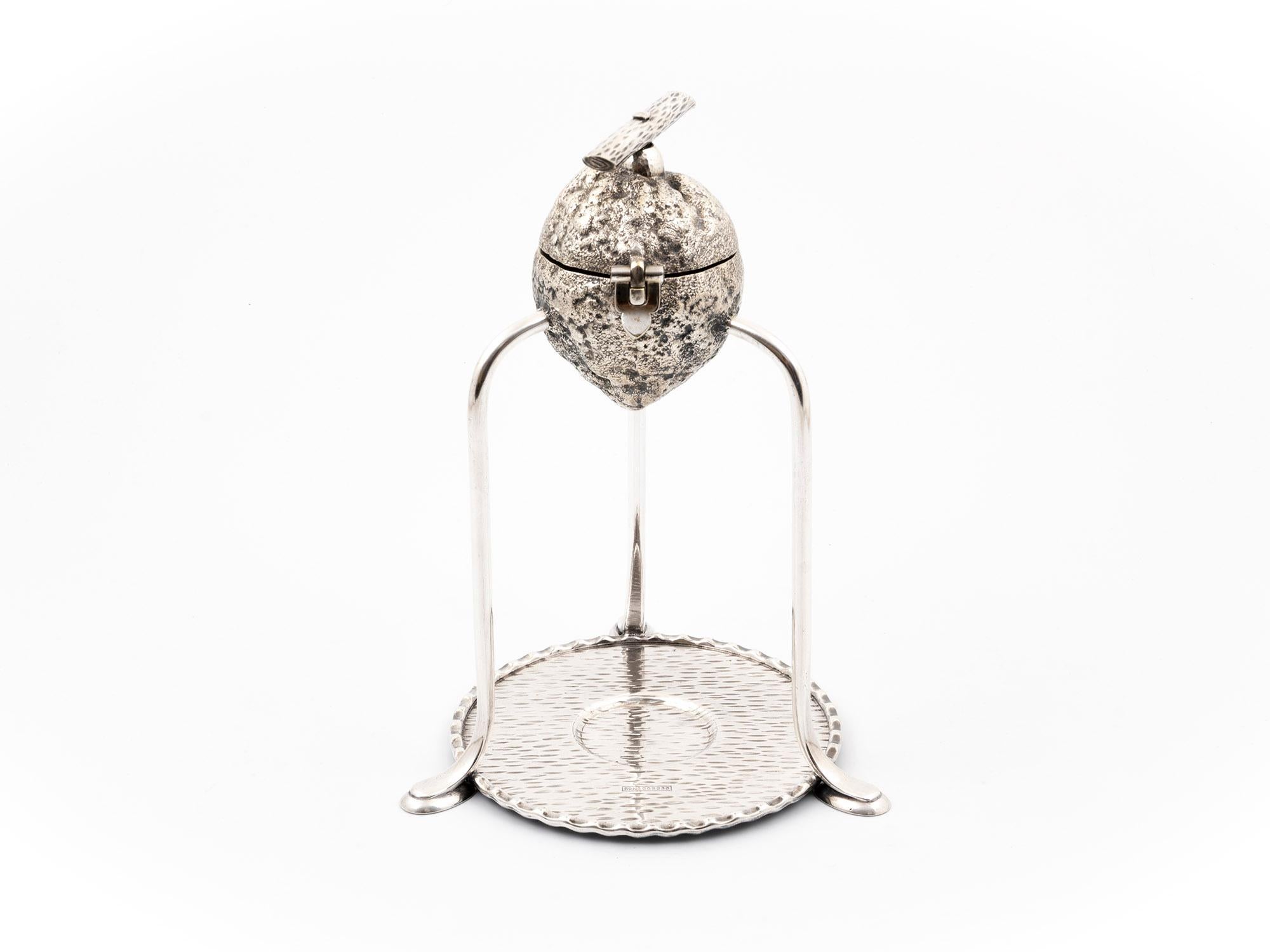 Silver-plated Hukin & Heath fruit squeezer. The squeezer has a turned wooden press with a screw handle in the style of a tree branch.

The body of the fruit squeezer has a registered design number: 203233. This number can also be found on the base