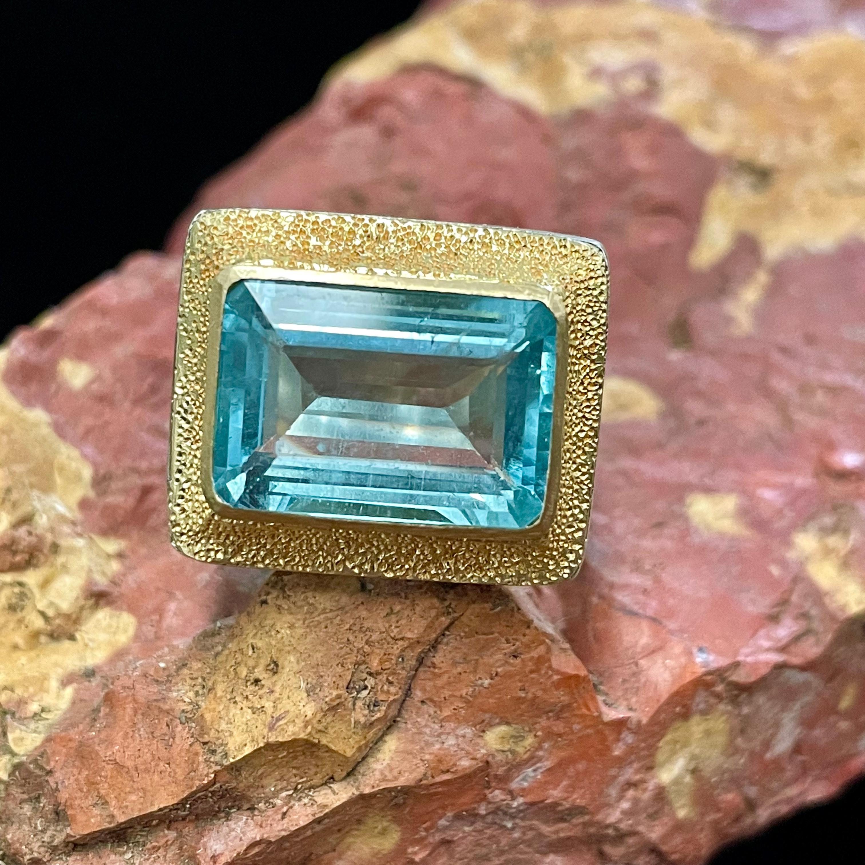 Una aguamarina brasileña facetada octogonal de 11 x 15 mm rodeada de oro texturizado a mano es la pieza central de esta creación en oro y plata de Steven Battelle. La caña de plata martillada está ligeramente dentada a los lados para que te resulte