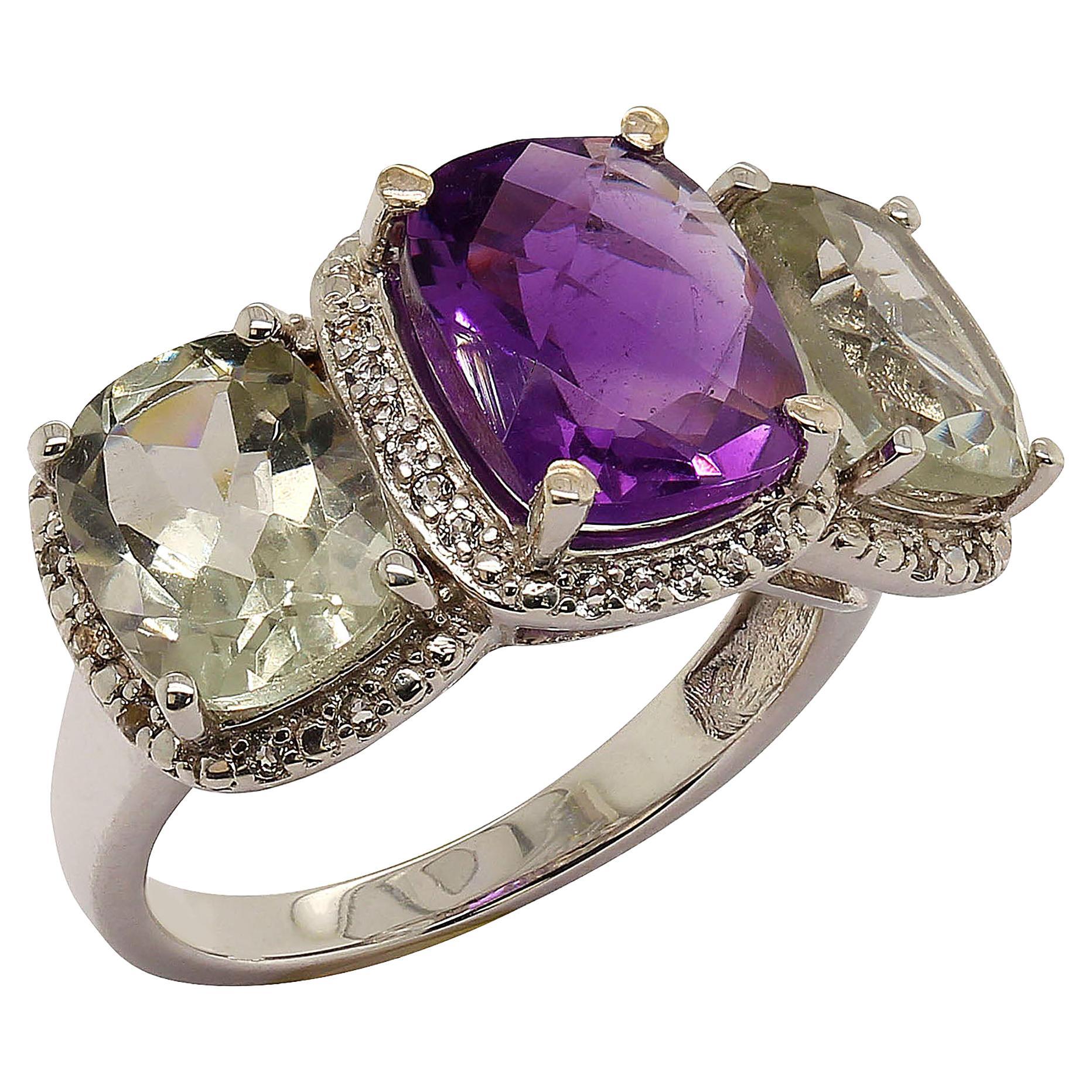 Custom designed striking three gemstone ring featuring a checkerboard cushion cut Amethyst center stone.  The side stones which equal 4. 52ct are sparkling green Praziolites, also cushion cuts.  Each gemstone is surrounded by a halo of granulated