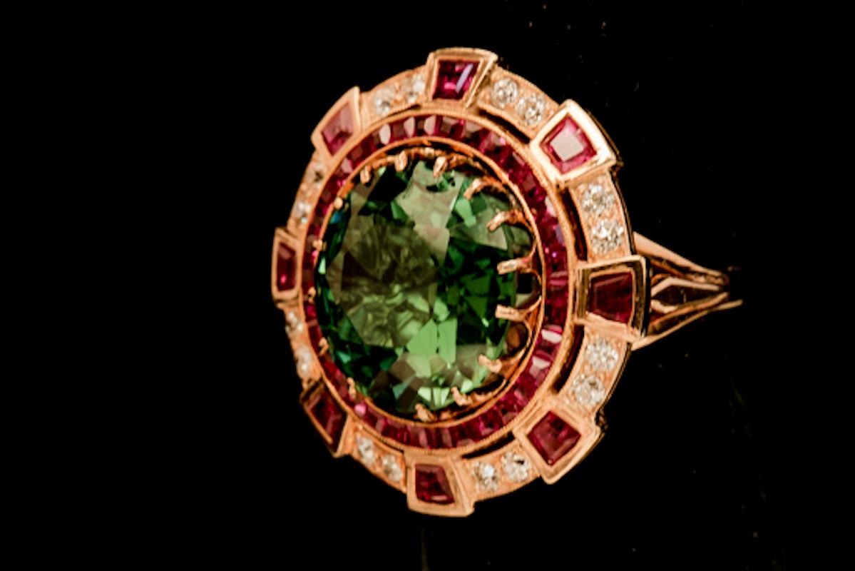A lady's 18k yellow gold, tourmaline, ruby, and diamond ring.  The stones are prong set and the center stone is a round faceted natural tourmaline having an estimated weight of 8.79 carats of very good quality, green color, medium tone, very well
