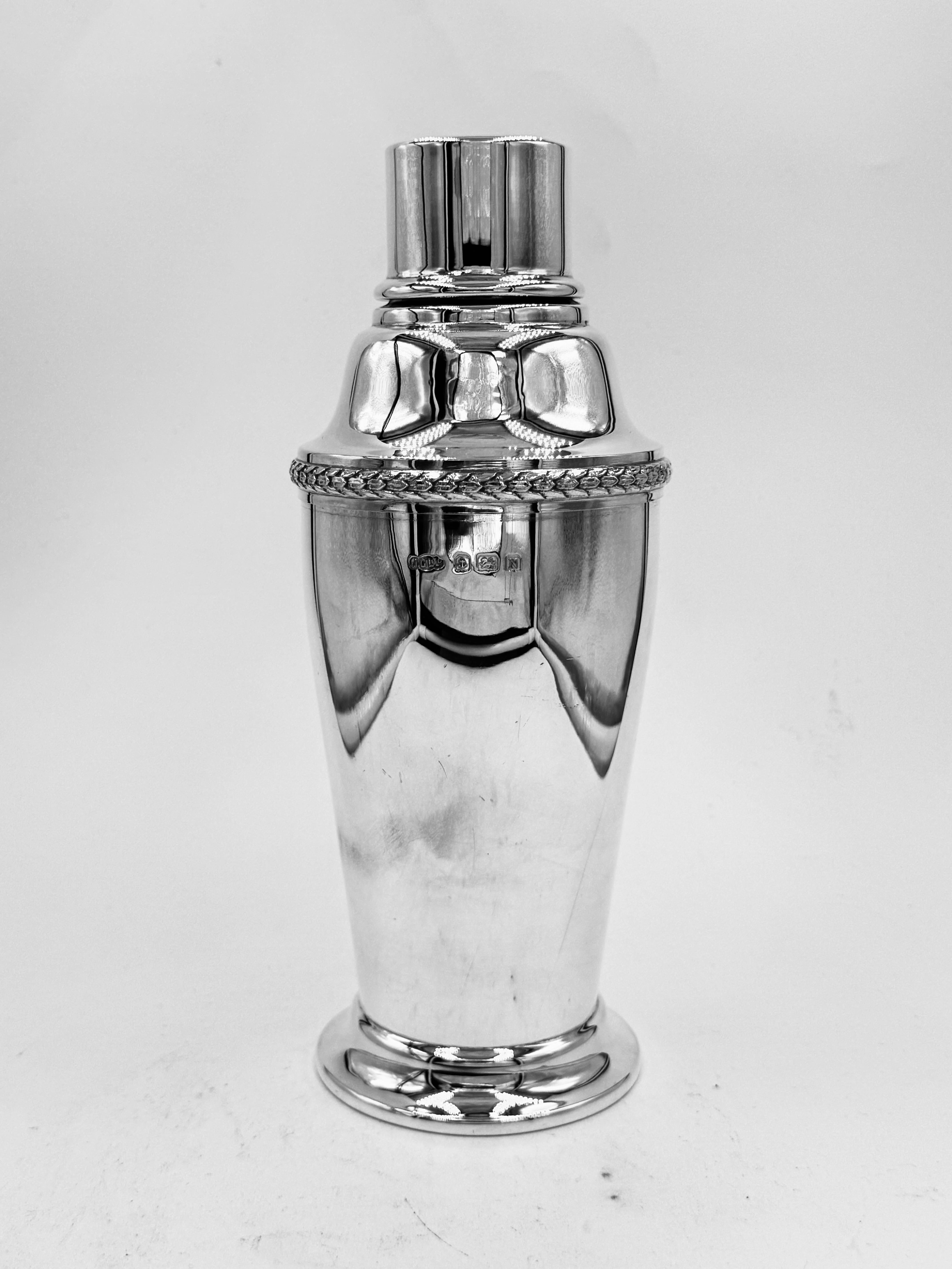 Cocktail Shaker aus englischem Sterlingsilber, hergestellt von der Firma J. Gloster Ltd. in Birmingham und gestempelt 1937.
Auf der ansonsten völlig glatten Oberfläche befindet sich ein einzelner, mit Weizenflocken verzierter Rand.


