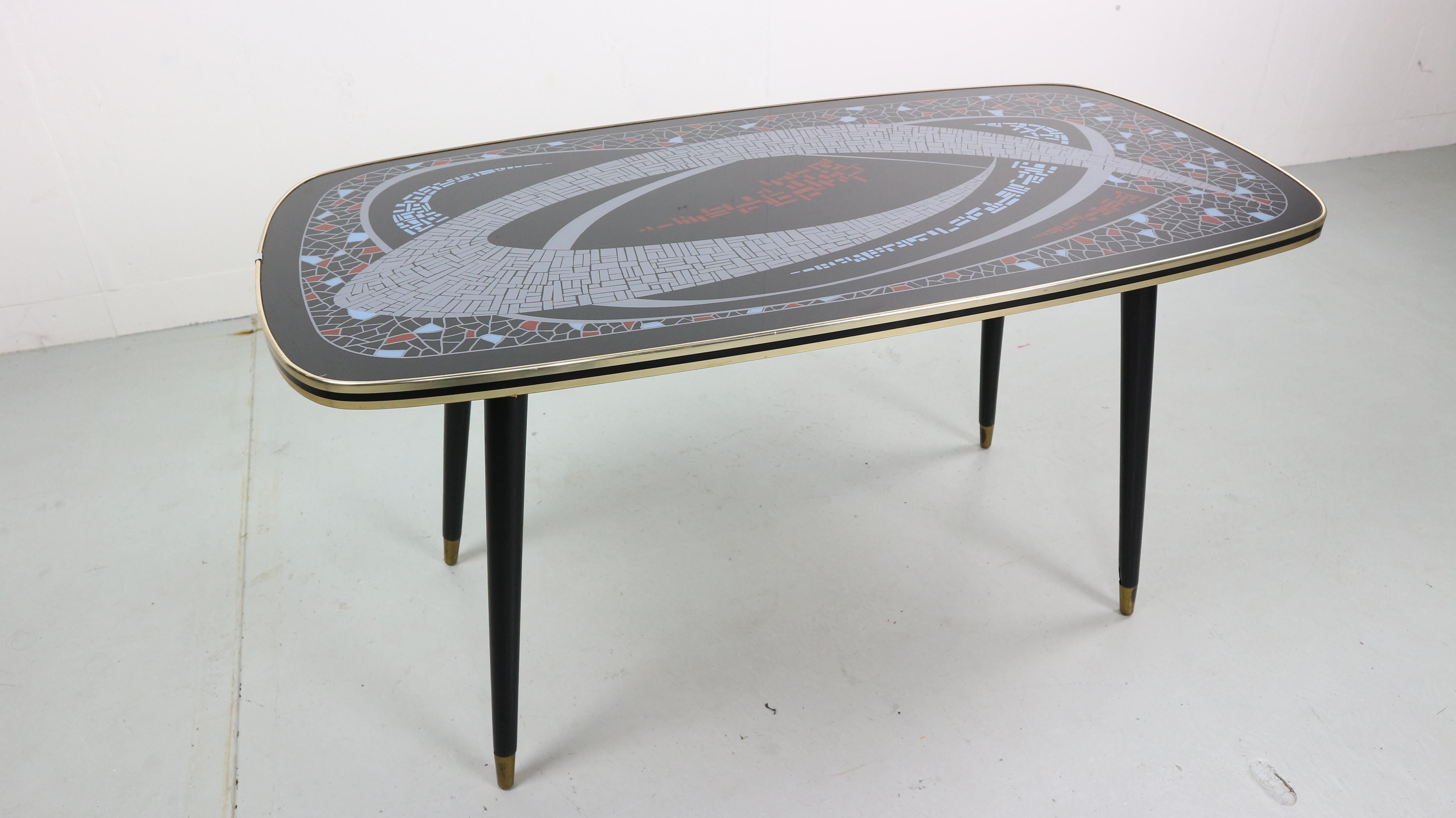 Very stylish and elegant black and brass game or coffee table on a wooden frame with slim brass feet and beautiful painted pattern glass top. 
France, 1950s.