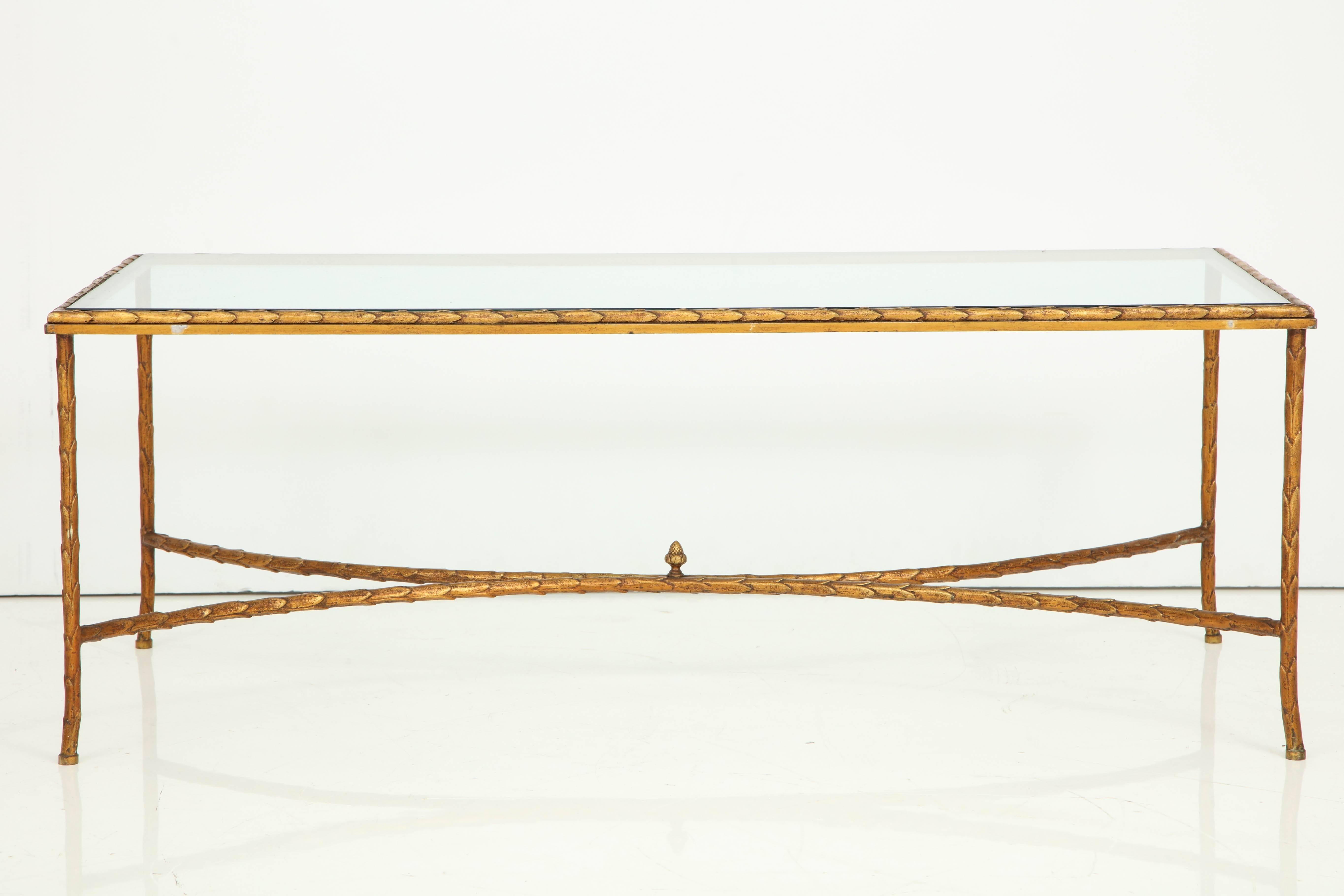 A gilt bronze cocktail table with a glass top attributed to Maison, Baguès, France. The glass top sits on the table frame with a leaf motif, characteristic of the elegance of Maison Baguès. The stretcher at base, composed of two curved elements, is