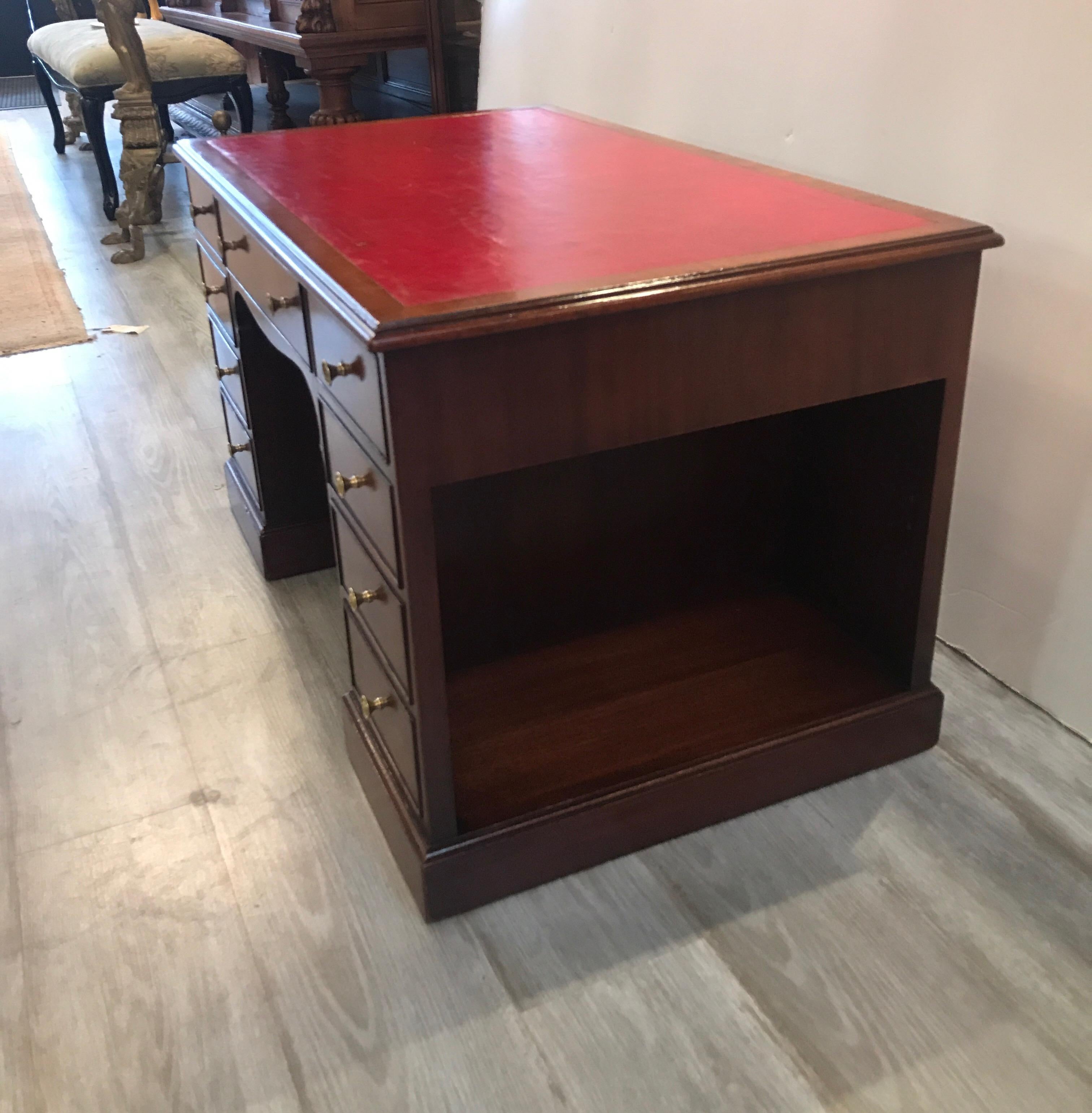 Whimsical mahogany and leather cocktail table in the form of an executive desk. Perfect for a study or library. The red leather top with three upper working drawers below. The side drawers are not function but there are two open storage compartments