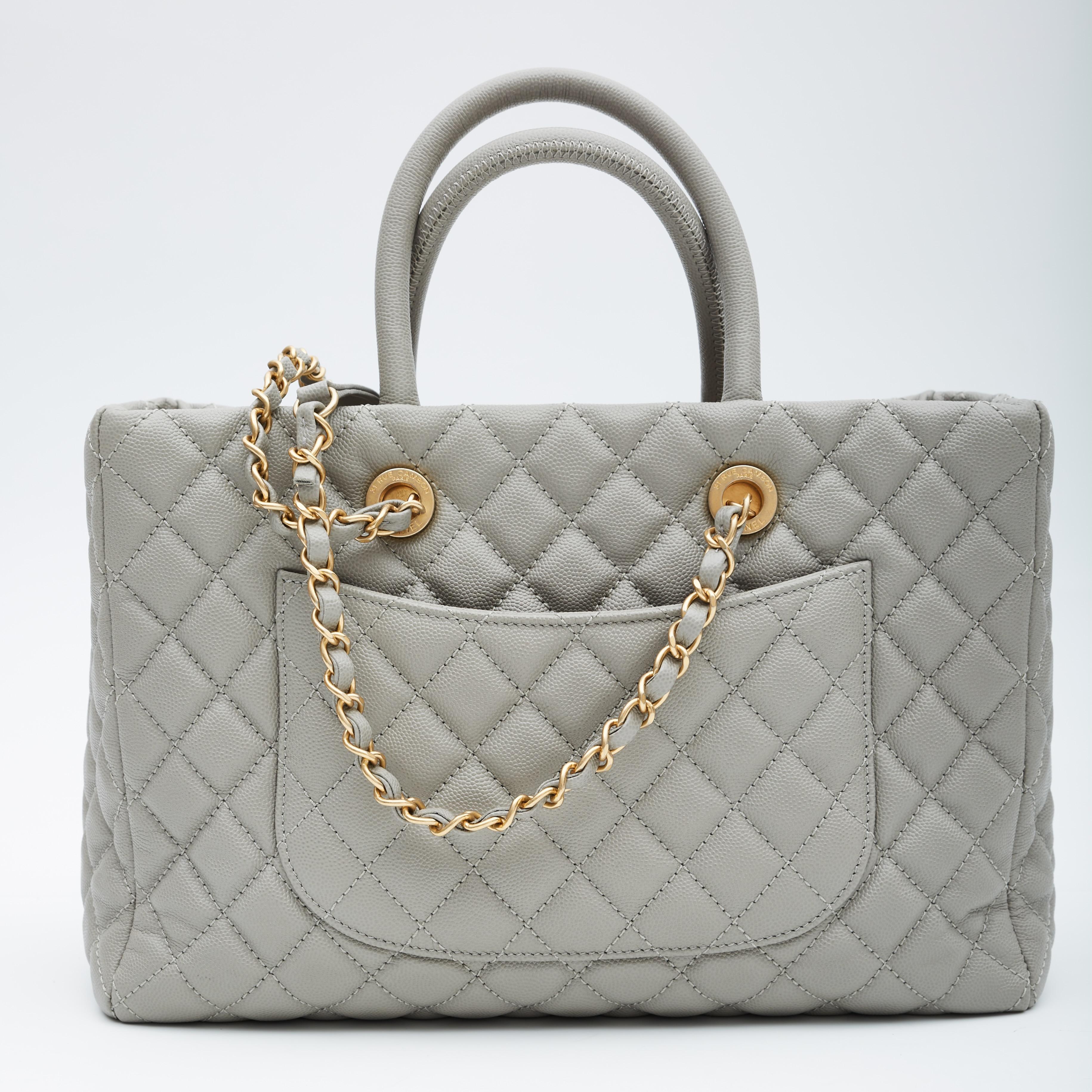 This handbag is made of diamond quilted gray caviar leather. This tote features leather threaded aged gold chain shoulder straps with shoulder pads, dual rolled leather top handles, an aged gold Chanel CC logo on the front, a flat pocket on the