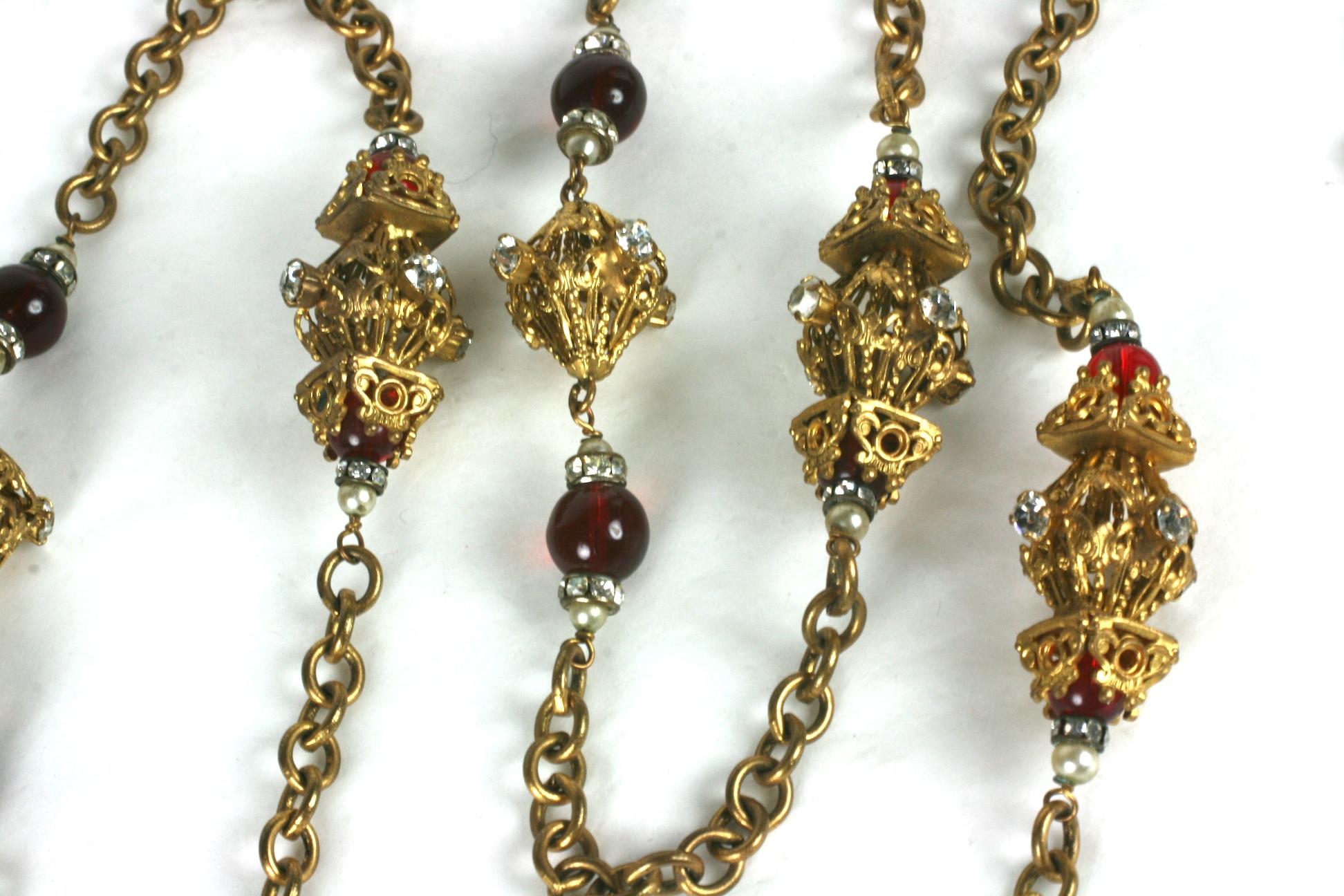 Early CoCo Chanel sautoir fabricated by Robert Goossens of Renaissance inspiration, composed of deep ruby pate de verre beads flanked by rondelles of crystal brilliants and small faux pearls. There are gilt filigree lantern shaped stations in two