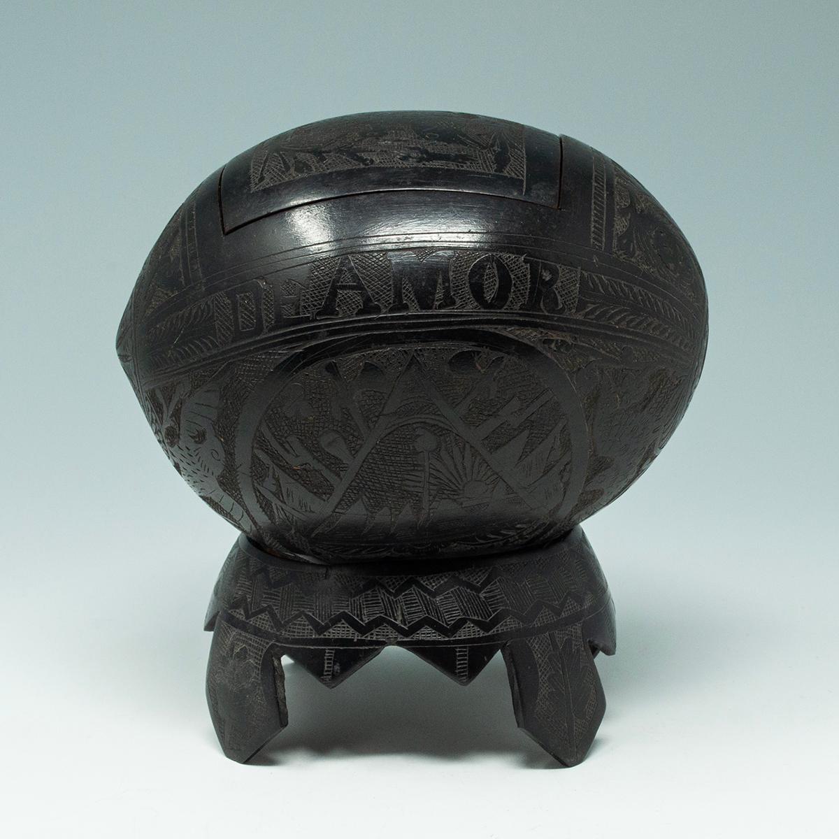 Coconut Bugbear Box/Tea Caddy by Unknown Sailor

A carved coconut bugbear in the form of a box with an unhinged lid with a carved image of a bird on a branch. Carved around the lid are the words REQUERDOS and DE AMOR, which translates as 