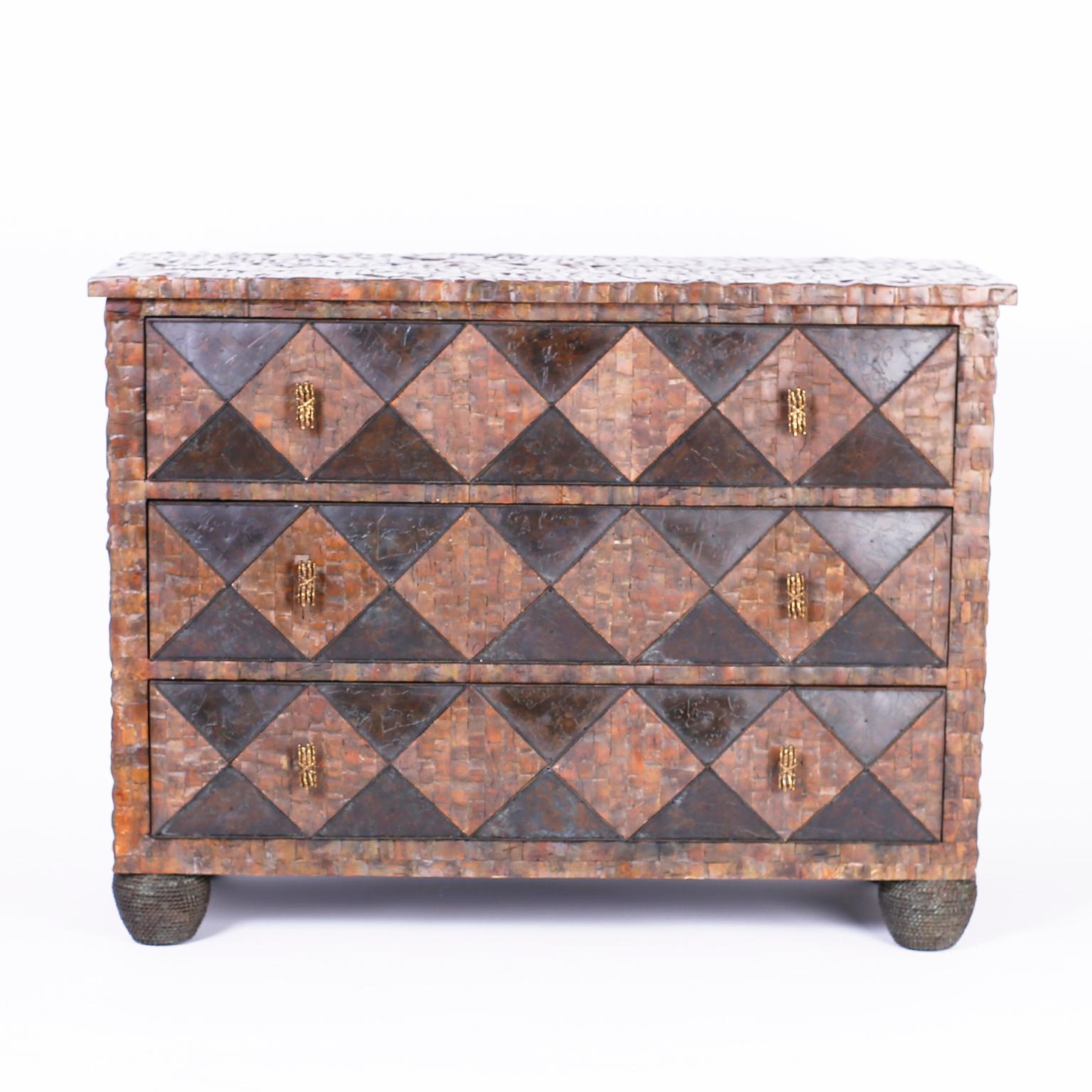 A three drawer chest or commode entirely clad with a coconut shell mosaic with harlequin drawer fronts and set on faux string bun feet. Signed Maitland-Smith in a drawer.