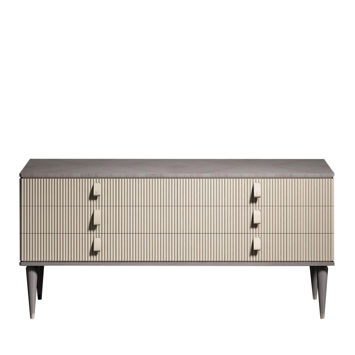 Distinguished for its clean edges and intricate panel detailing, this dresser exudes timeless elegance. Made entirely of wood, the rectangular frame has an inlay veneer at the top, brass-accented conical feet, and base in grey finish. The central