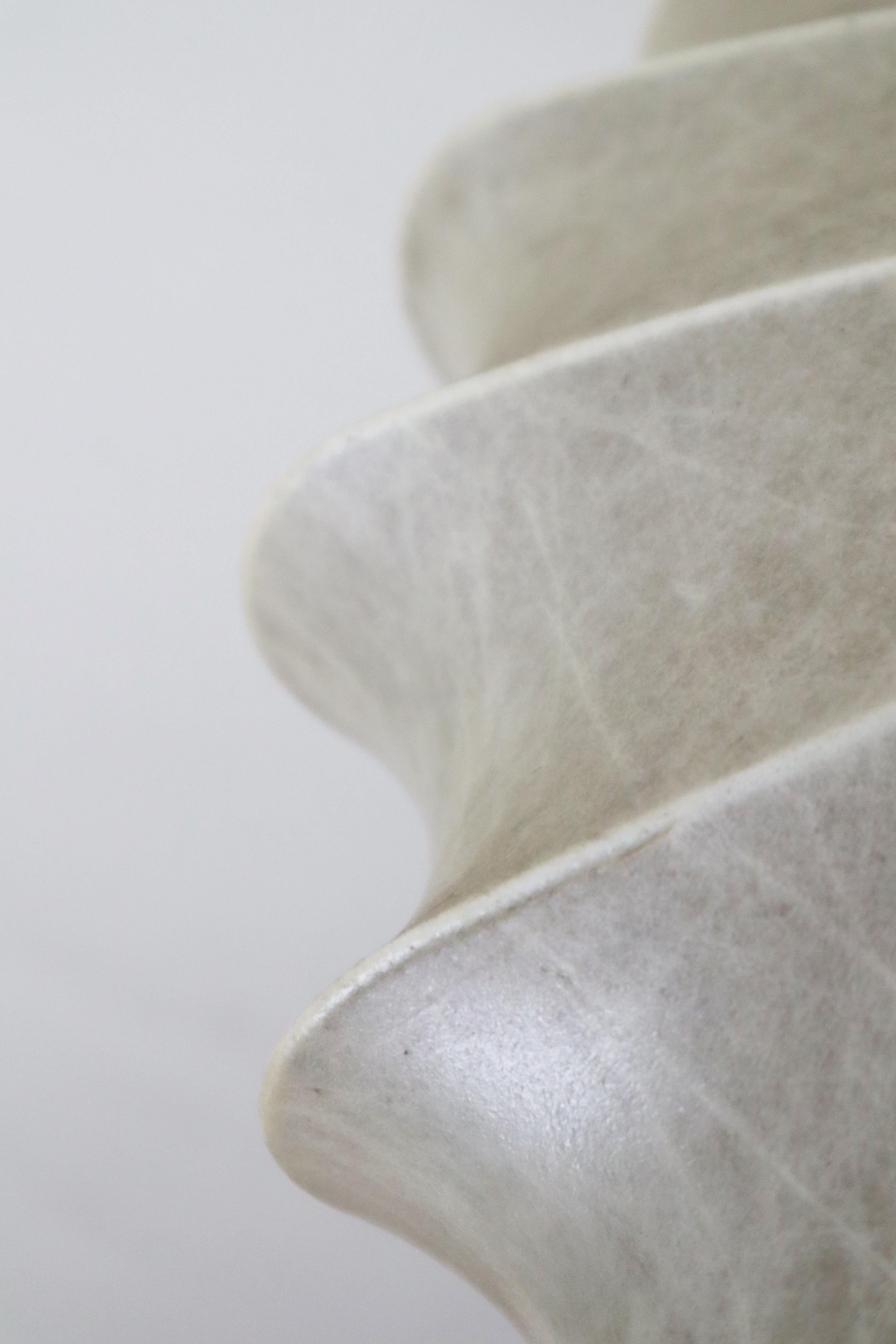 Cette lampe suspendue Cocoon est d'une beauté unique grâce à son design élégant et intemporel. L'abat-jour en forme de cocon est drapé avec art sur le cadre en fil de fer, ressemblant à une fleur. Le fleuron en bois de teck situé au sommet de la