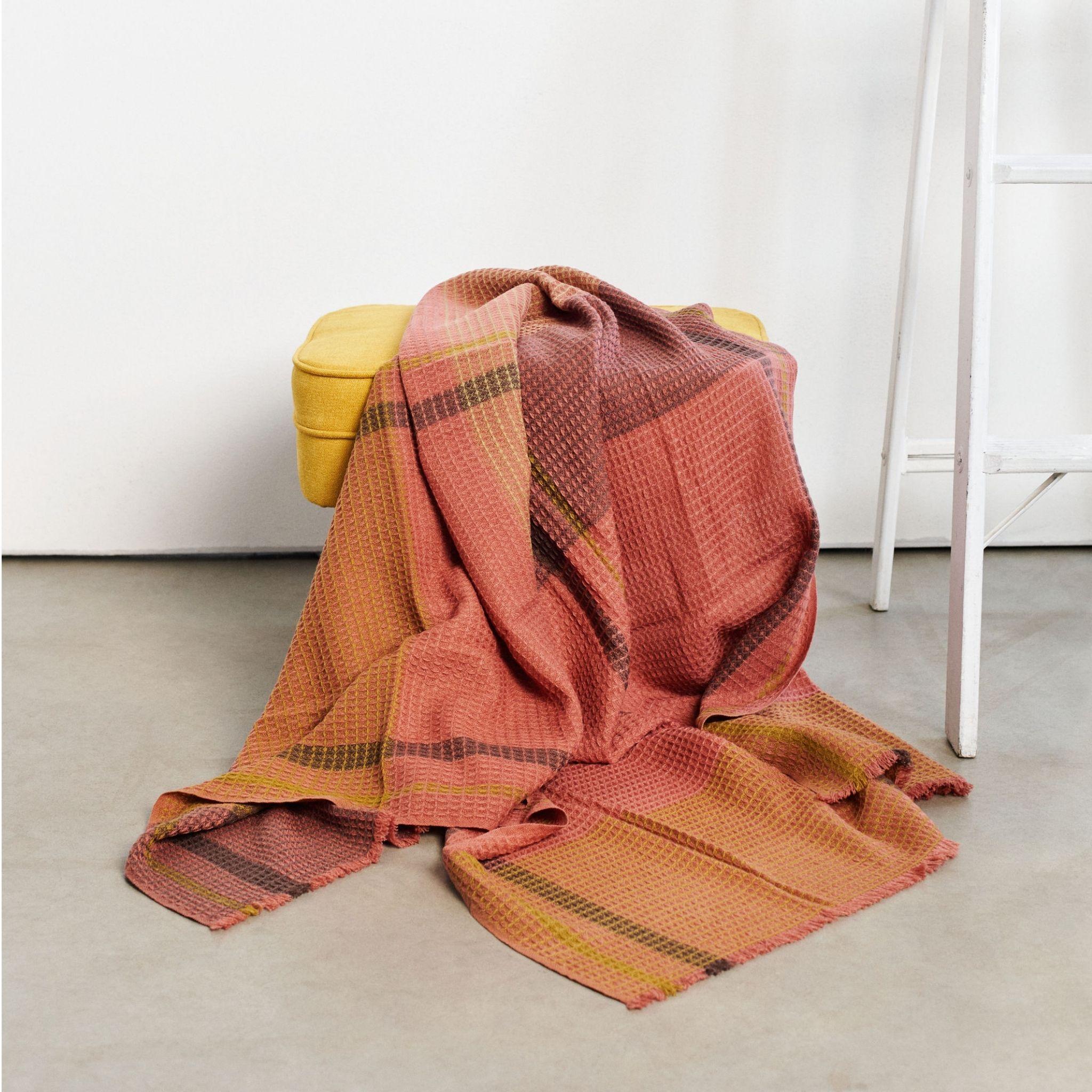 Cocoon is a meticulous handwoven throw in waffle weave pattern by artisans in Nepal. The design of this serene throw with a earthy pop of color ,  is made up of subtle textured checks pattern in waffle weave.Edges of this throw are short and neat