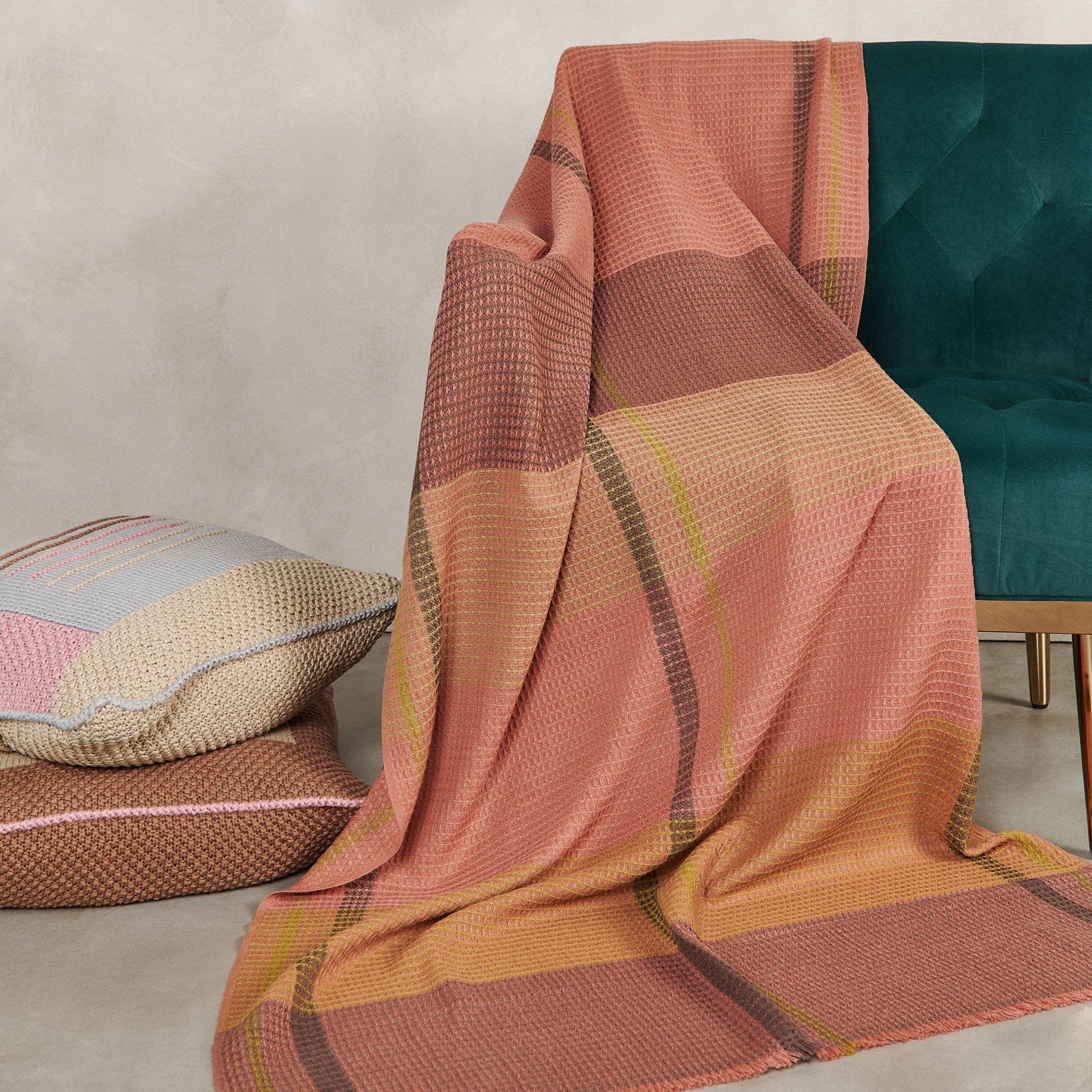 Cocoon es una manta meticulosamente tejida a mano con un patrón de gofre por artesanos de Nepal. El diseño de esta manta serena con un toque de color terroso ,  Está confeccionada con un sutil estampado de cuadros texturizados en tejido waffle. Los