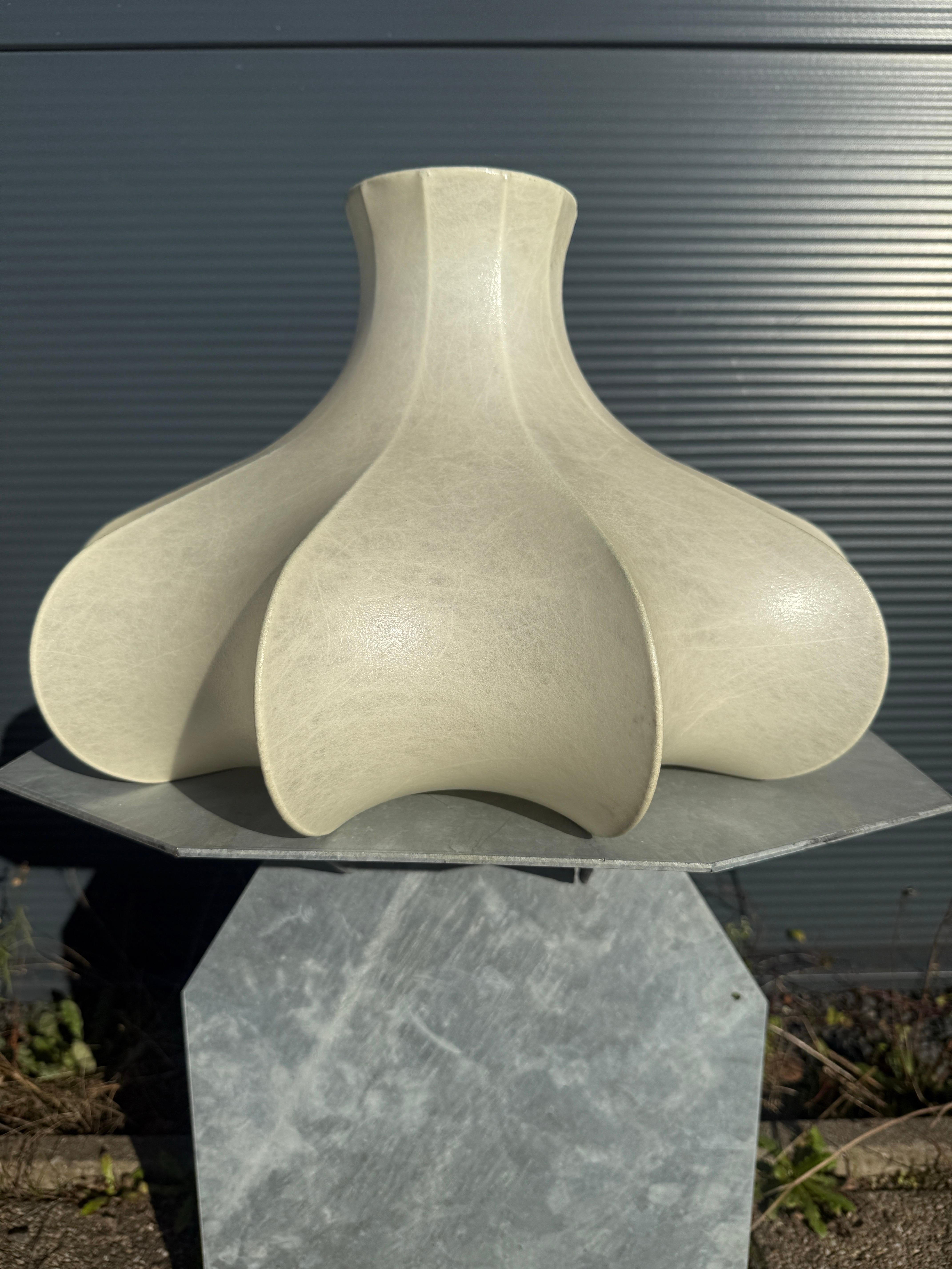 La Lámpara Cocoon es una obra maestra del diseño moderno de mediados de siglo, célebre por su uso innovador de materiales y formas orgánicas. Achille Gastiglioni, en colaboración con su hermano Pier Giacomo Castiglioni, diseñó las primeras lámparas