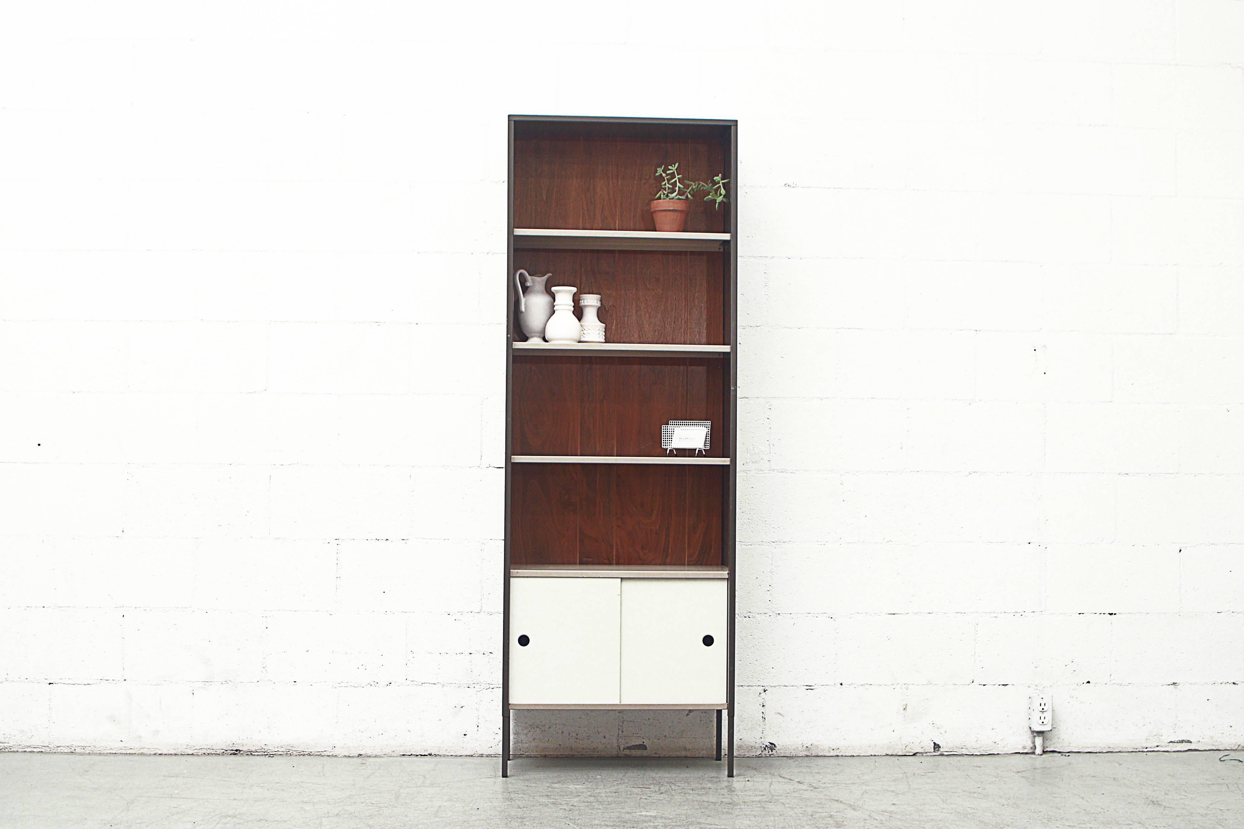 Brown enameled metal cabinet with wood paneled backing, beige enameled metal shelves over a small cabinet with bone white enameled metal sliding doors. Visible wear, scratching and minimal paint loss to some of the shelves and doors. Condition is