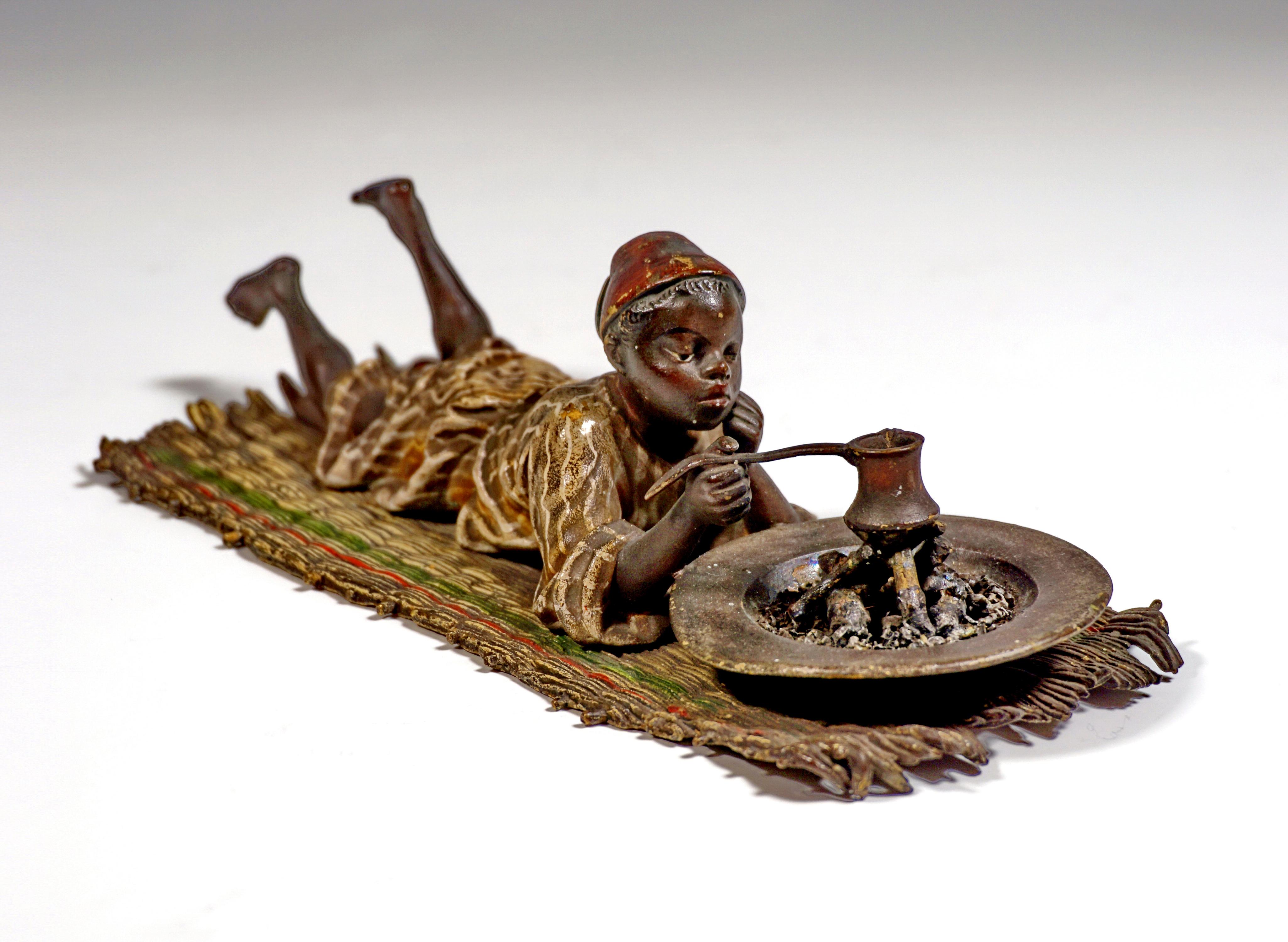 Excellent Piece of Viennese Bronze Art around 1900:
Oriental boy with fez in a long, striped robe lying on his belly on a straw mat, supporting his head with his left hand, making coffee in a small, long-handled vessel on a brazier.
The figure is