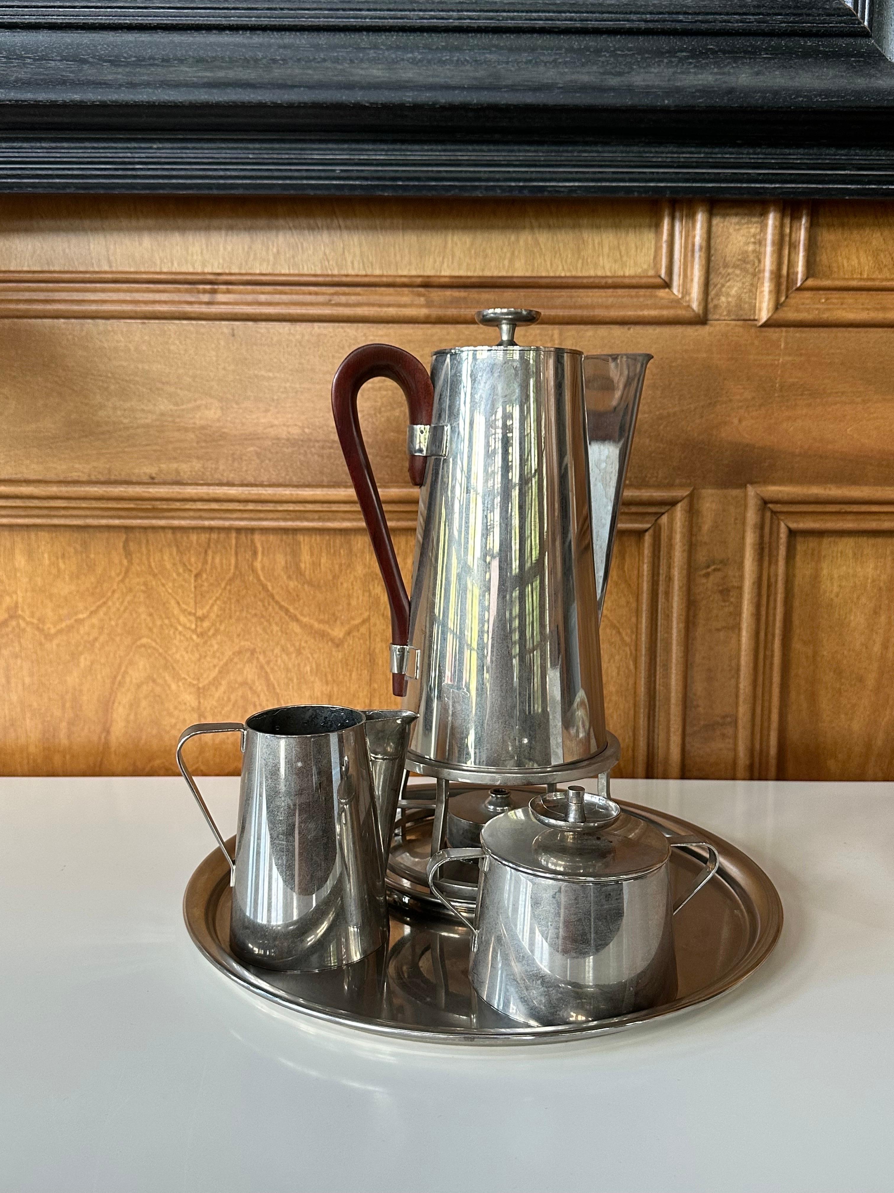 A coffee or tea serving set designed by Tommi Parzinger for Dorlyn Silversmith. The set is made of heavy brass and newly rechromed in a nickle finish. It consists of a pitcher with wood handle equipped with a heater, a creamer, a lidded sugar and a