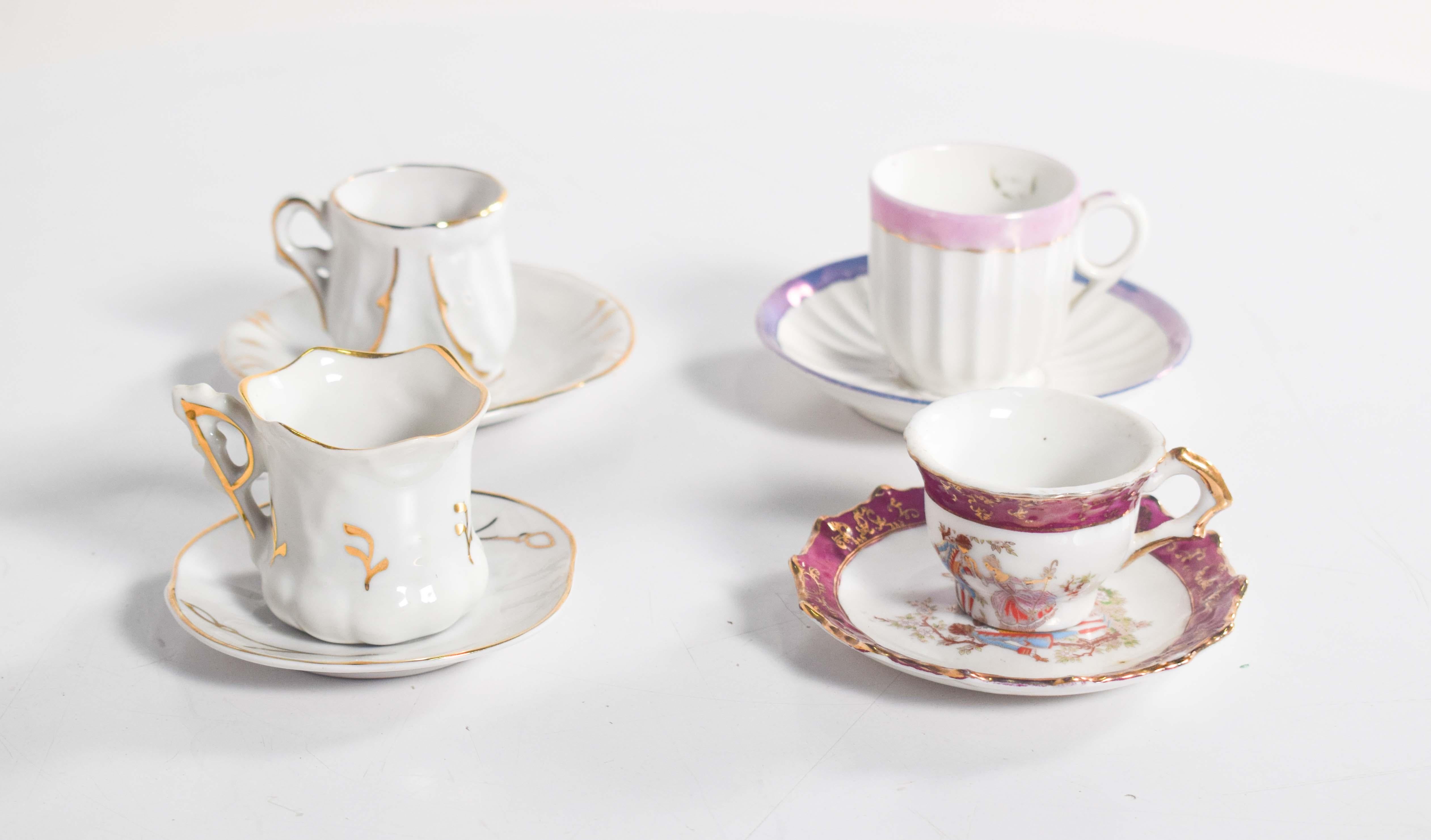 This delightful coffee set consists of four unique and artistic cups with matching saucers, each showcasing a distinct design and charm. Two of the cups are crafted from fine white porcelain and elegantly decorated with delicate gold accents,