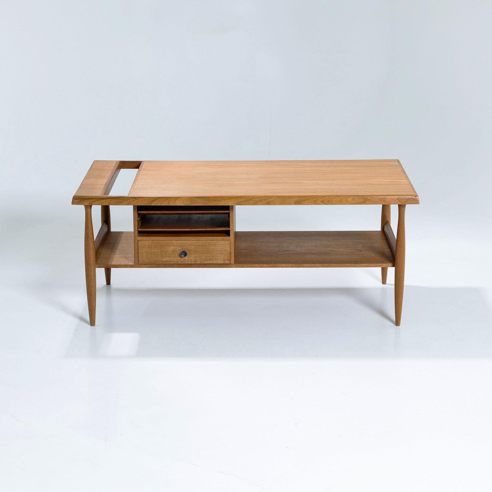Rectangular coffee table with a practical magazine shelf and a drawer, supported by sleek tapered legs. The design is further enhanced by additional storage compartments above the drawer, offering both functionality and an intriguing asymmetrical