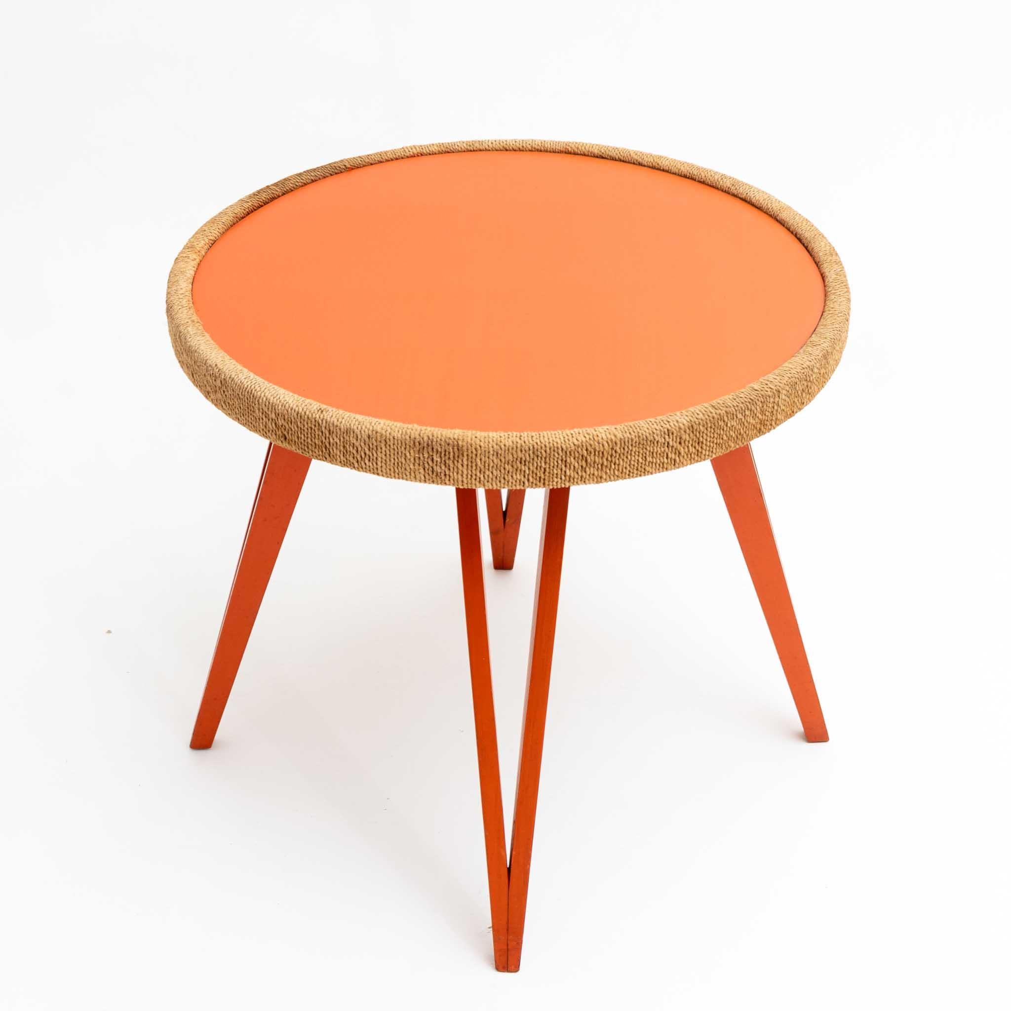 Couchtisch auf Haarnadelbeinen aus orange-rot gefärbtem Holz und runder Tischplatte mit Kordelrand aus Naturfaser. Die Tischplatte ist ebenfalls in einem Orangeton gehalten. Der Tisch wird dem italienischen Designer Augusto Romano (1918-2001)