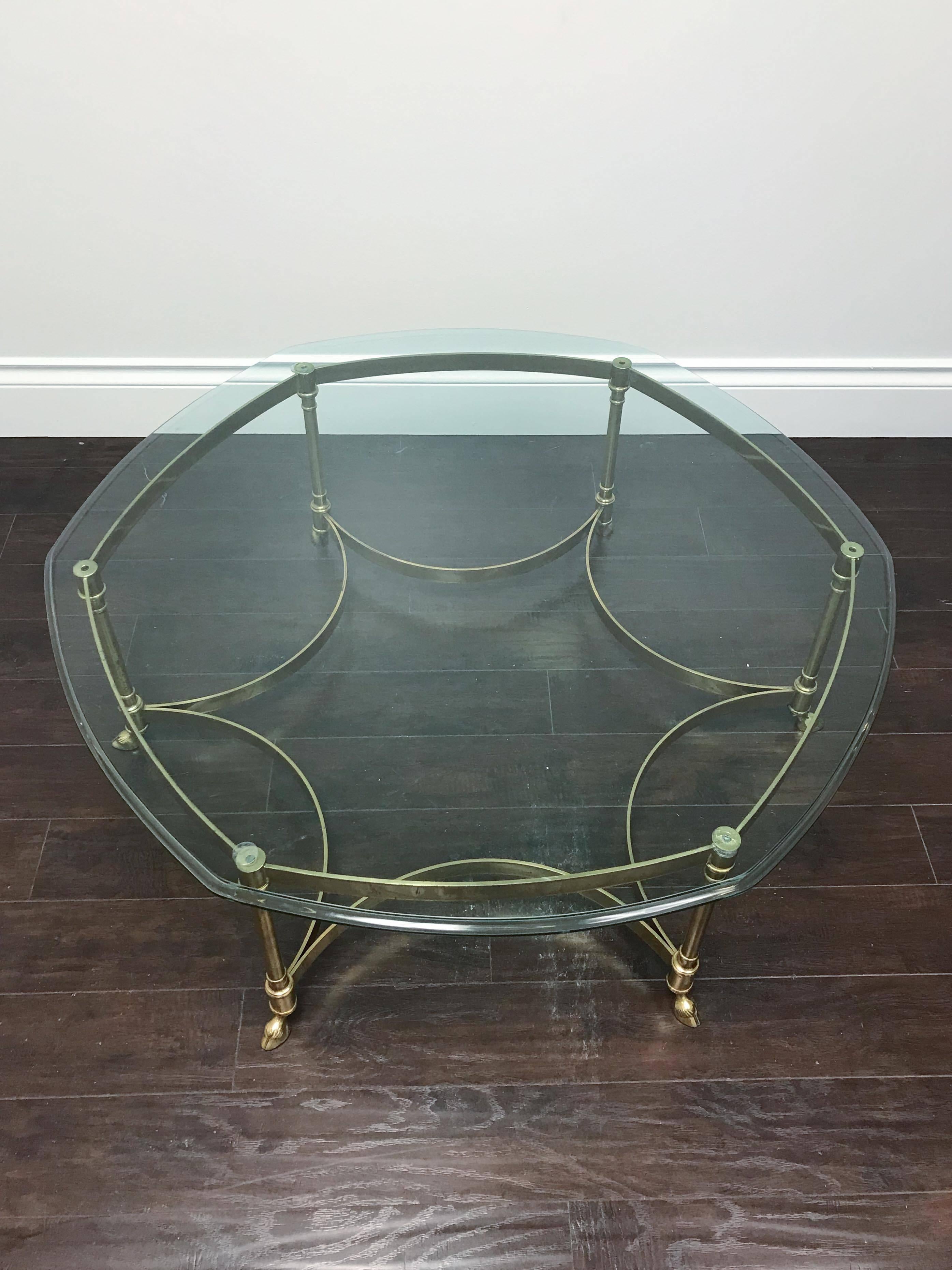 A gorgeous brass hexagonal coffee table with hoof feet and bevelled glass top attributed to La Barge. Original condition with natural patina on base and some surface scratching to glass top.