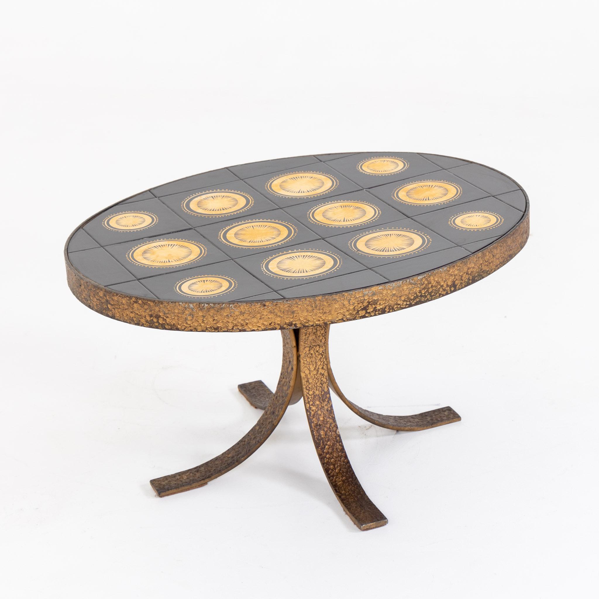 Small coffee table with oval table top and hammered metal frame. The table top is made of square black ceramic discs with golden radiating decorations. The metal base is attributed Pierluigi Colli.