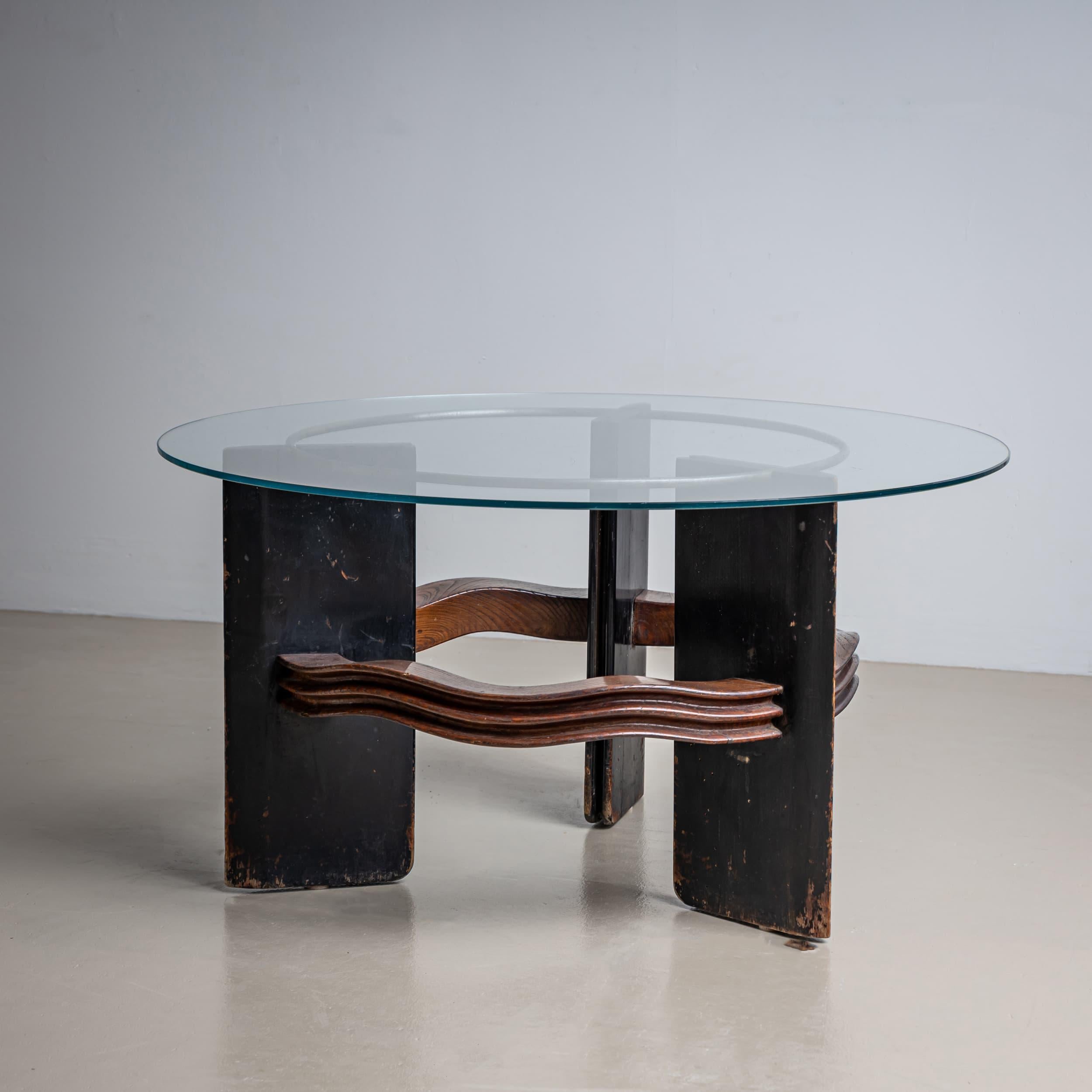 This iconic round coffee table attributed to Italian designer Vittorio Valabrega from the 1930s features an elegant glass top and a three-legged wooden base. The legs are connected by wave-shaped struts, reflecting the unique design language of