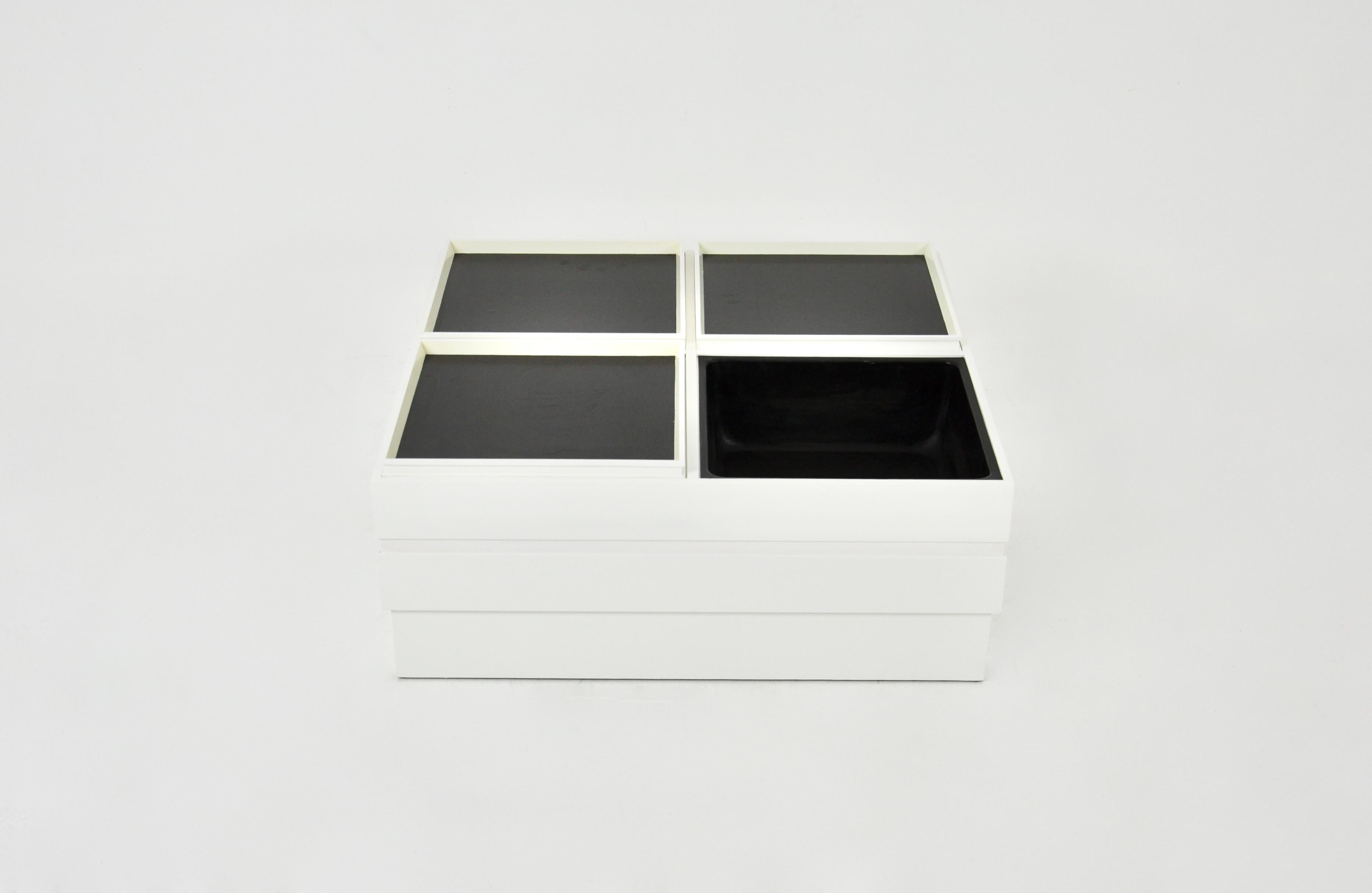 Table basse en bois blanc avec 4 compartiments de rangement. Il y a 3 plateaux, un noir et un blanc, et un plateau. L'ensemble est modulaire. Usure due au temps et à l'âge de la table basse.