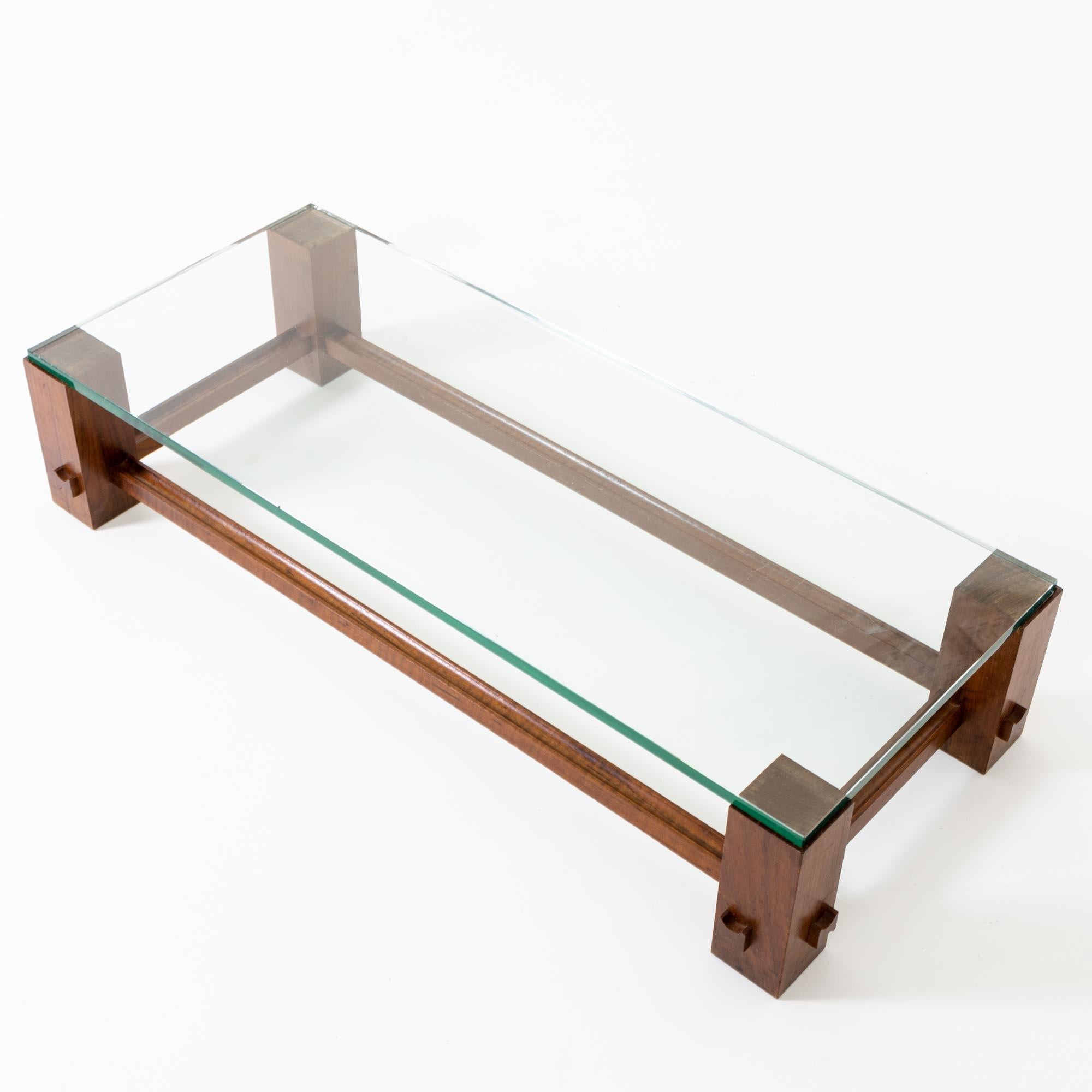 Table basse rectangulaire sur un soubassement en hêtre teinté brun foncé recouvert d'une épaisse vitre. Les étais sont constitués de lattes de bois profilées en forme de U.