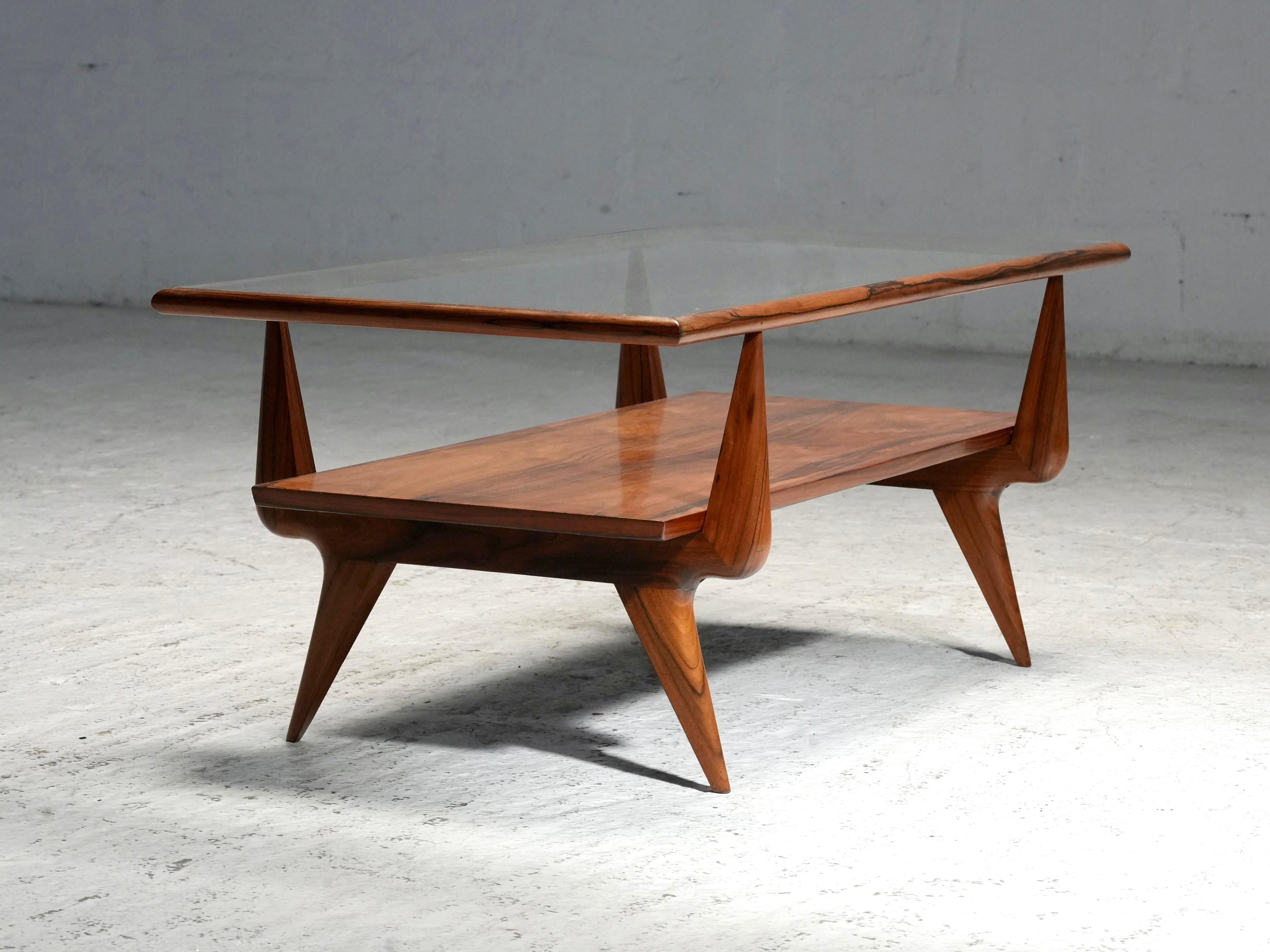 Cette table basse de Giuseppe Scapinelli, fabriquée dans les années 1950, témoigne de l'importance accordée par le designer aux matériaux et aux formes. La table combine un plateau en verre avec une base sculpturale en bois, probablement fabriquée