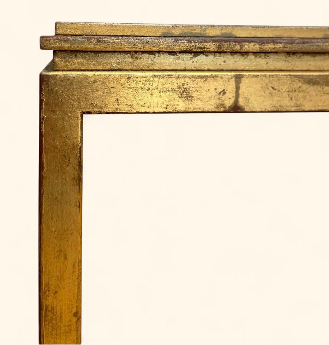 Mesa de centro con tablero rectangular de losa de cristal blanco revestida de metal patinado dorado y carmín.

Patas esquineras con patas acampanadas.  Bonita pátina de época.

Algunas marcas en el dorado y en las esquinas correspondientes a la