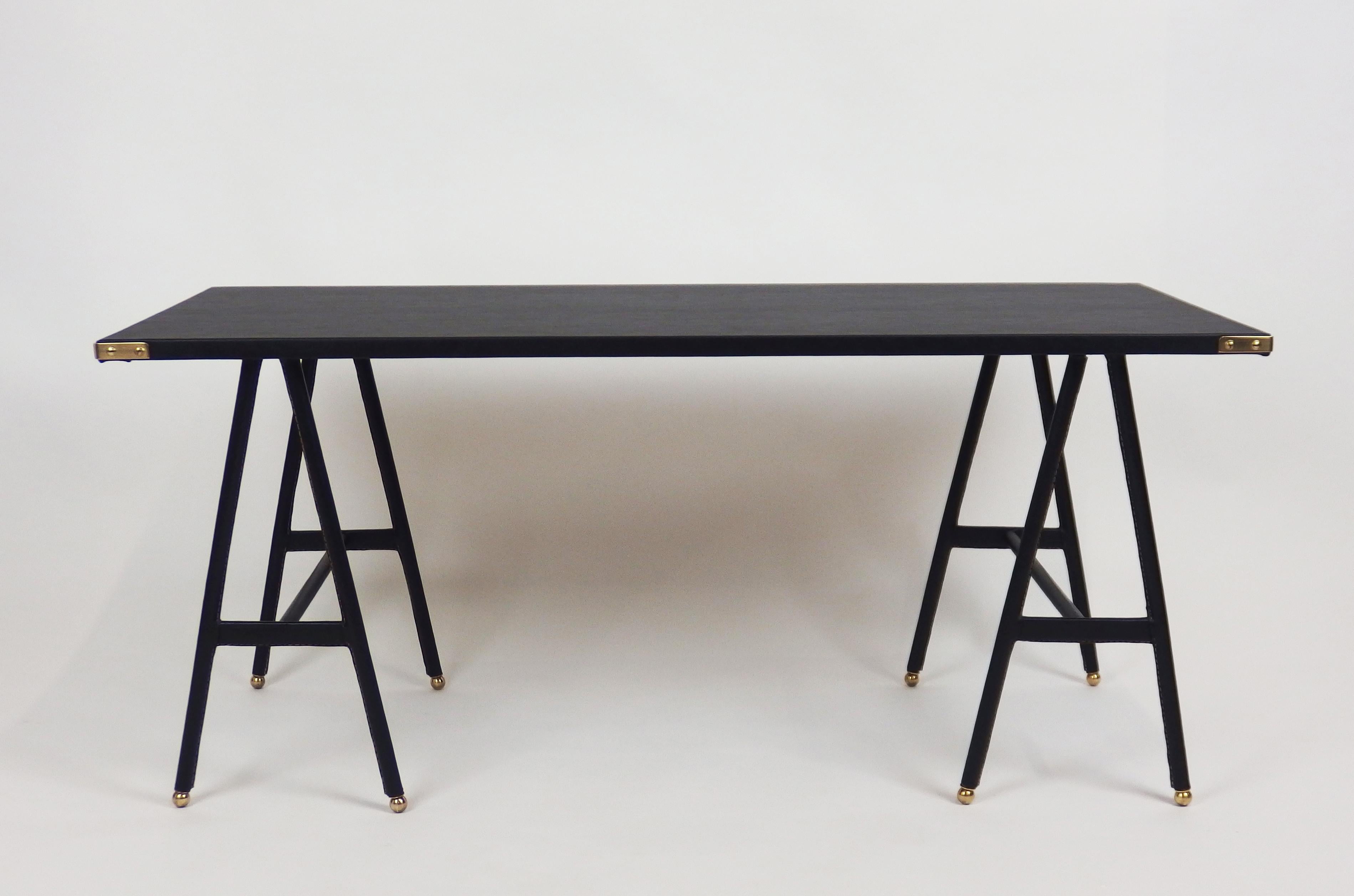 A black stitched leather and faux leather trestle coffee table by Jacques Adnet.The legs are in stitched leather and the top is in skai with brass corners.