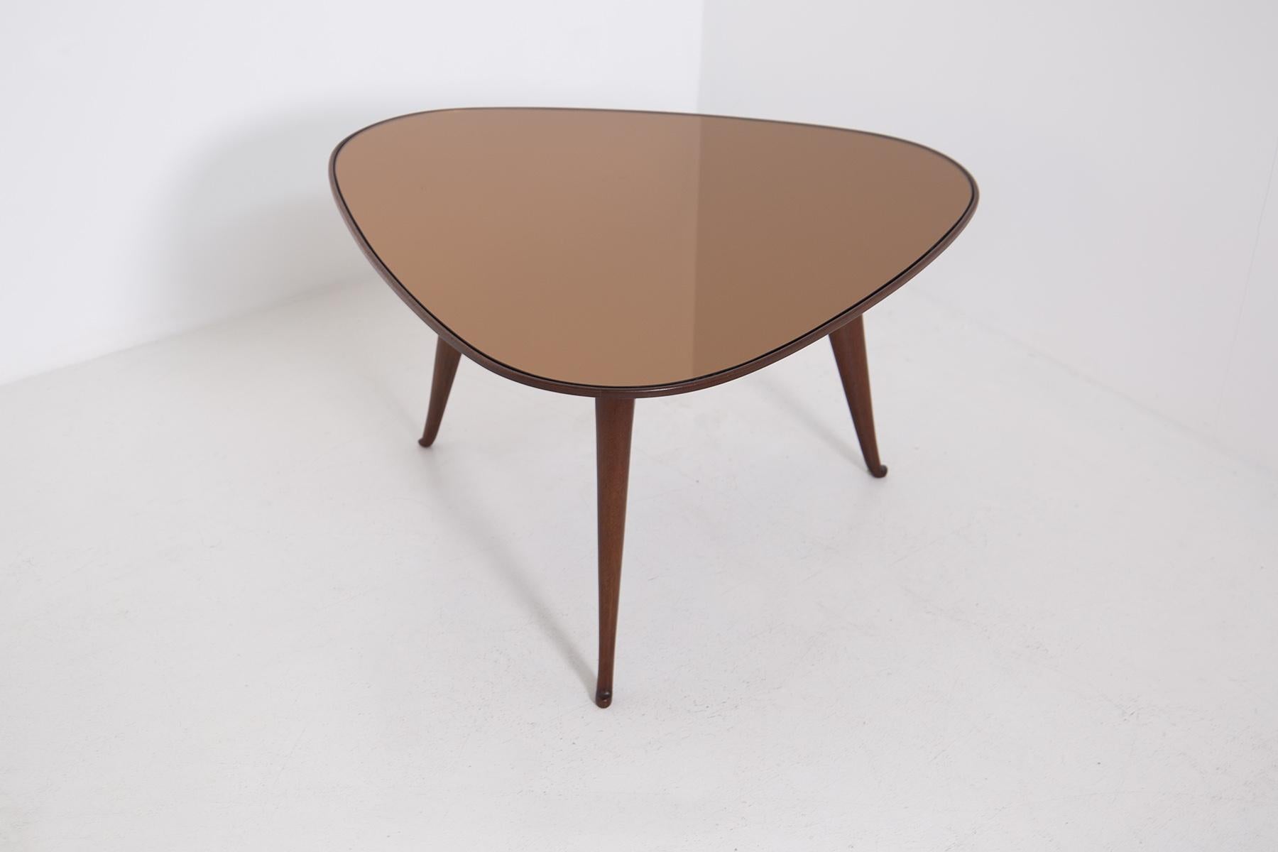 Elegant coffee table by Osvaldo Borsani from the 1950s. The coffee table is made of walnut wood with a triangular shape. Its three supporting legs have slightly curled feet at the bottom. The table top is made of dark orange mirrored glass,