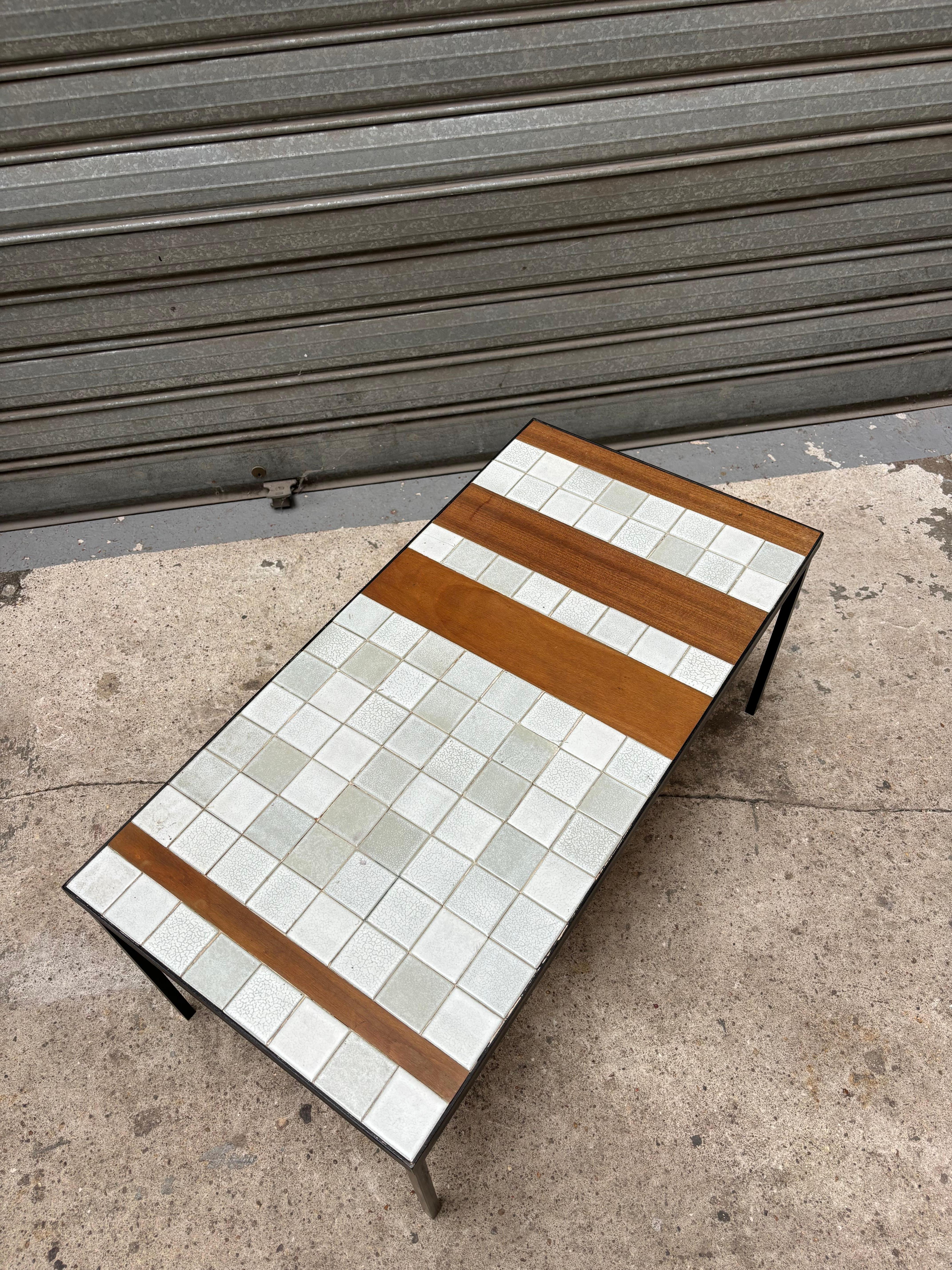 Roger CAPRON (1922-2006) Table basse de la série T, circa 1962, à plateau rectangulaire orné de carreaux en céramique gris et blanc et de trois lames en teck disposé sur une structure et métal laque noir formant le piètement H. : 38 cm. - L. : 83