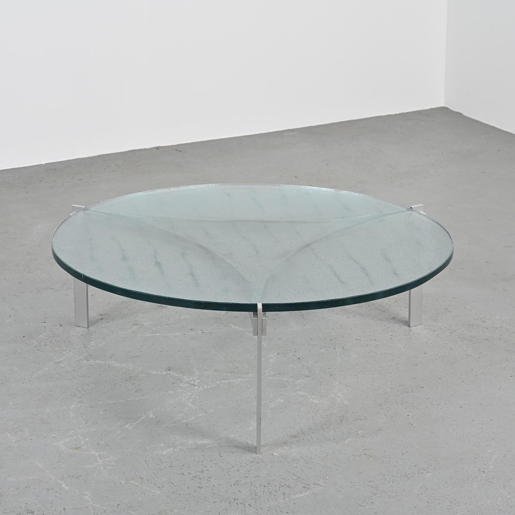 A coffee table by Teo Jakob, a rare find from the 1960s, will add a touch of vintage charm to any space.

This low, three-legged table is made of aluminum, with interconnected plates forming its base. It is topped with a thick glass top cast on a