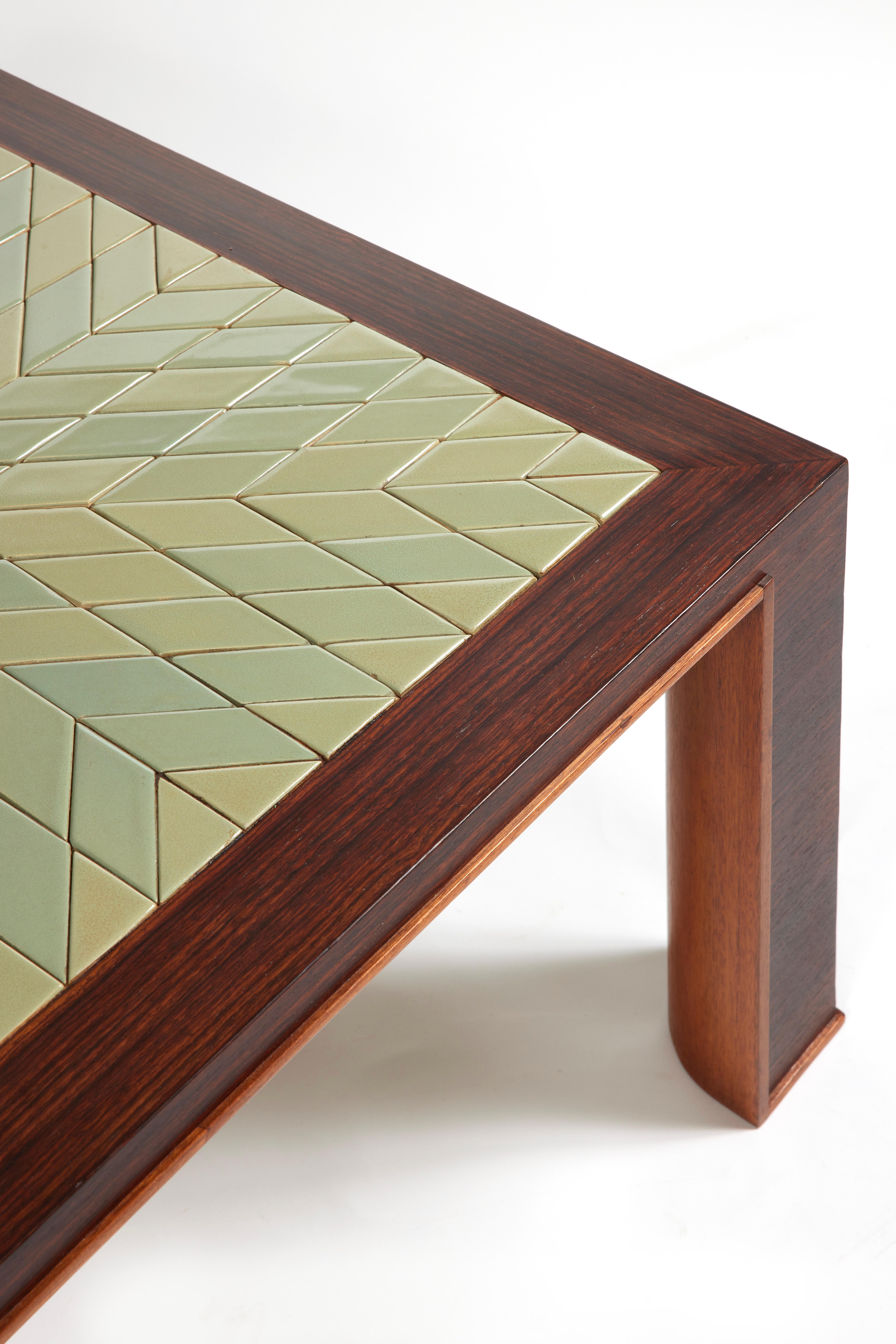 Table basse en placage de bois de rose avec plateau carré incorporant des carreaux de céramique émaillés verts avec un motif d'étoiles rayonnantes.
Jambes d'angle avec jambe droite à l'extérieur et arrondie à l'intérieur soulignée par un petit