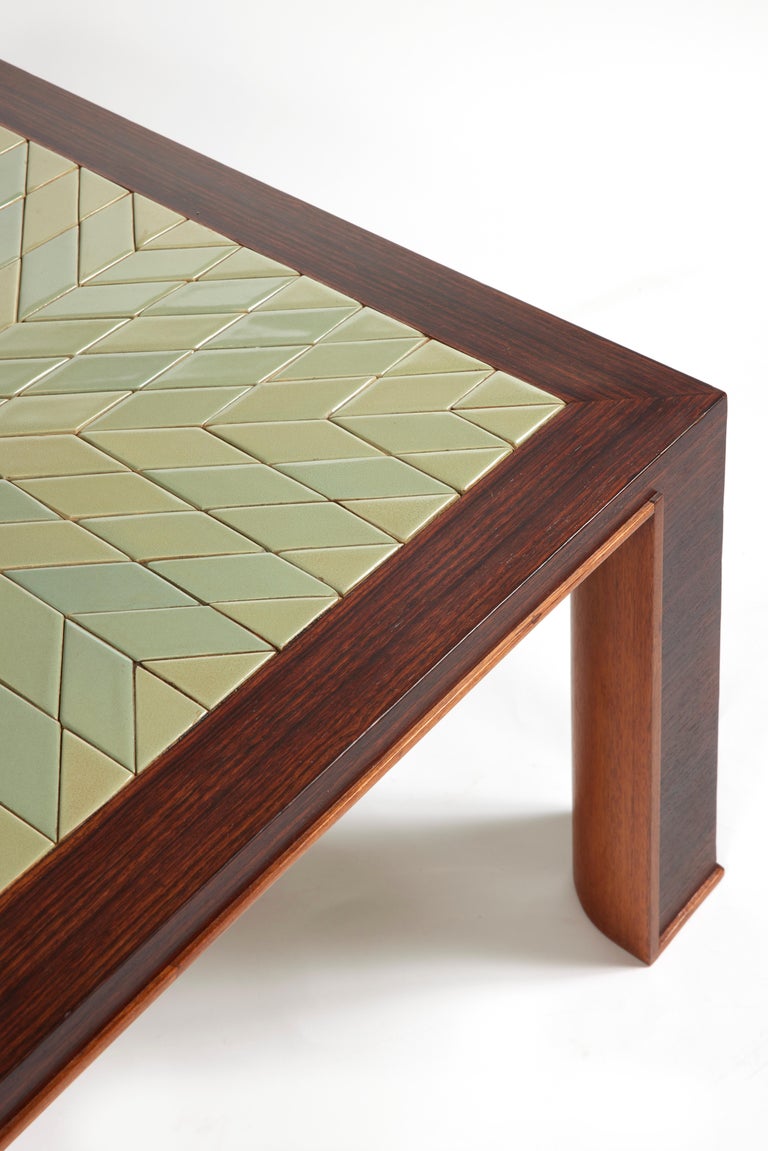 Rosewood veneer coffee table with square top incorporating green enameled ceramic tiles with a radiating star pattern.
Corner legs with straight leg on the outside and rounded on the inside underlined by a small rush.
The work of Jacques ADNET &