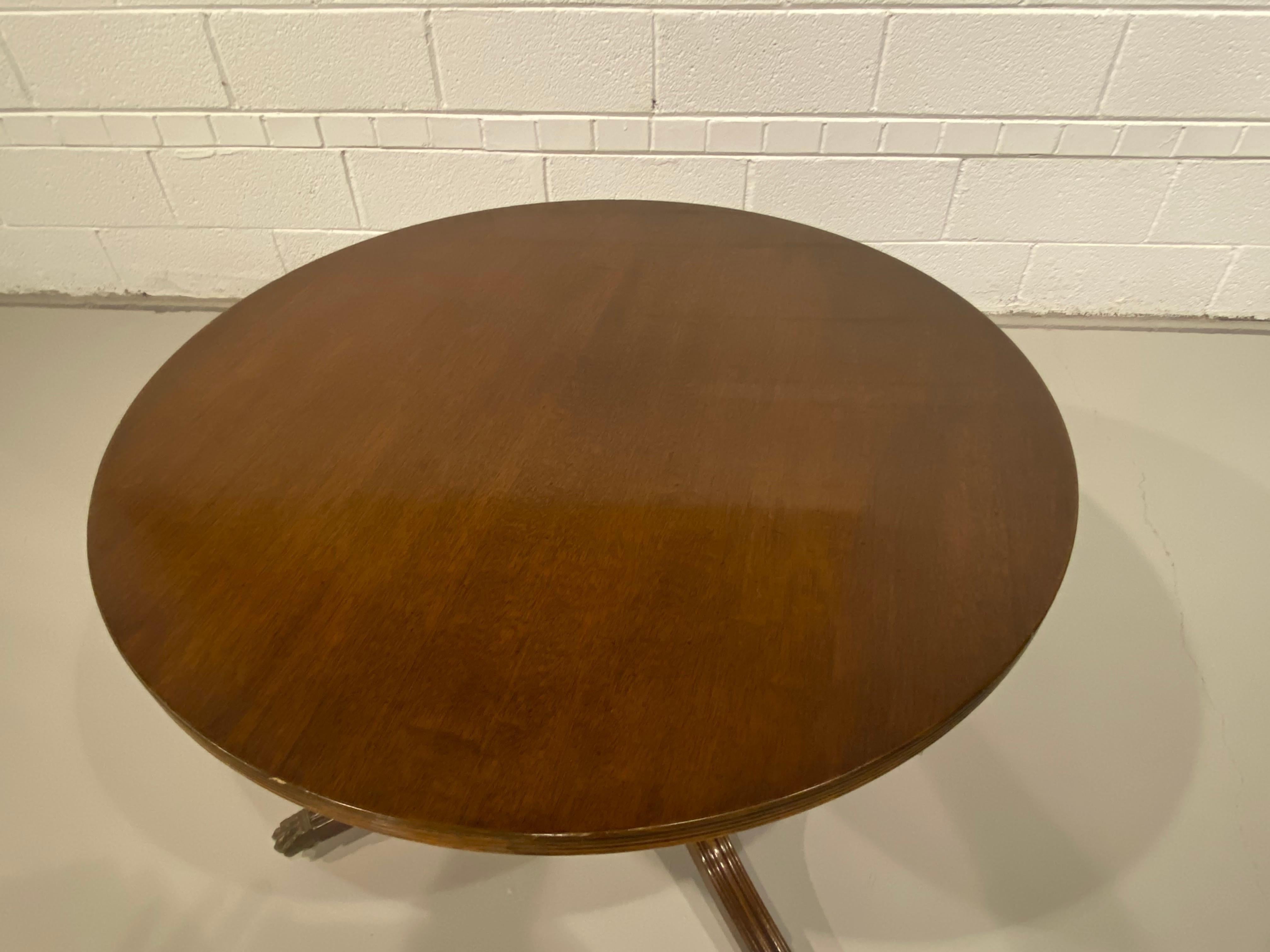 A round single pedestal Regency style mahogany pedestal coffee table or cocktail table with a reeded edge, made in England. The base is supported on the traditional brass claw toe caps with brass casters.