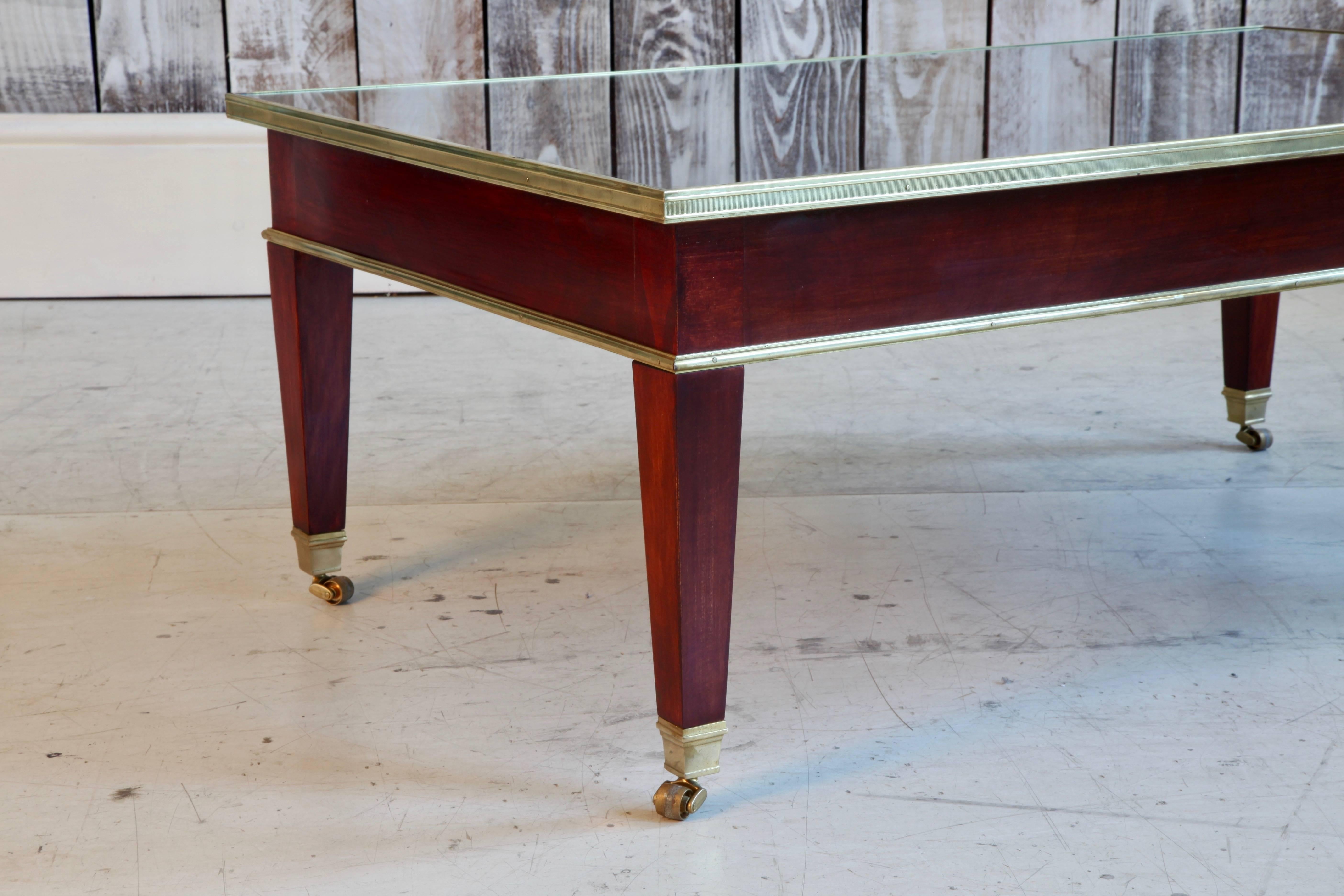 Table basse dans le style de la Maison Jansen, plateau en verre avec placage en acajou.
Bordure et pieds en bronze.
 