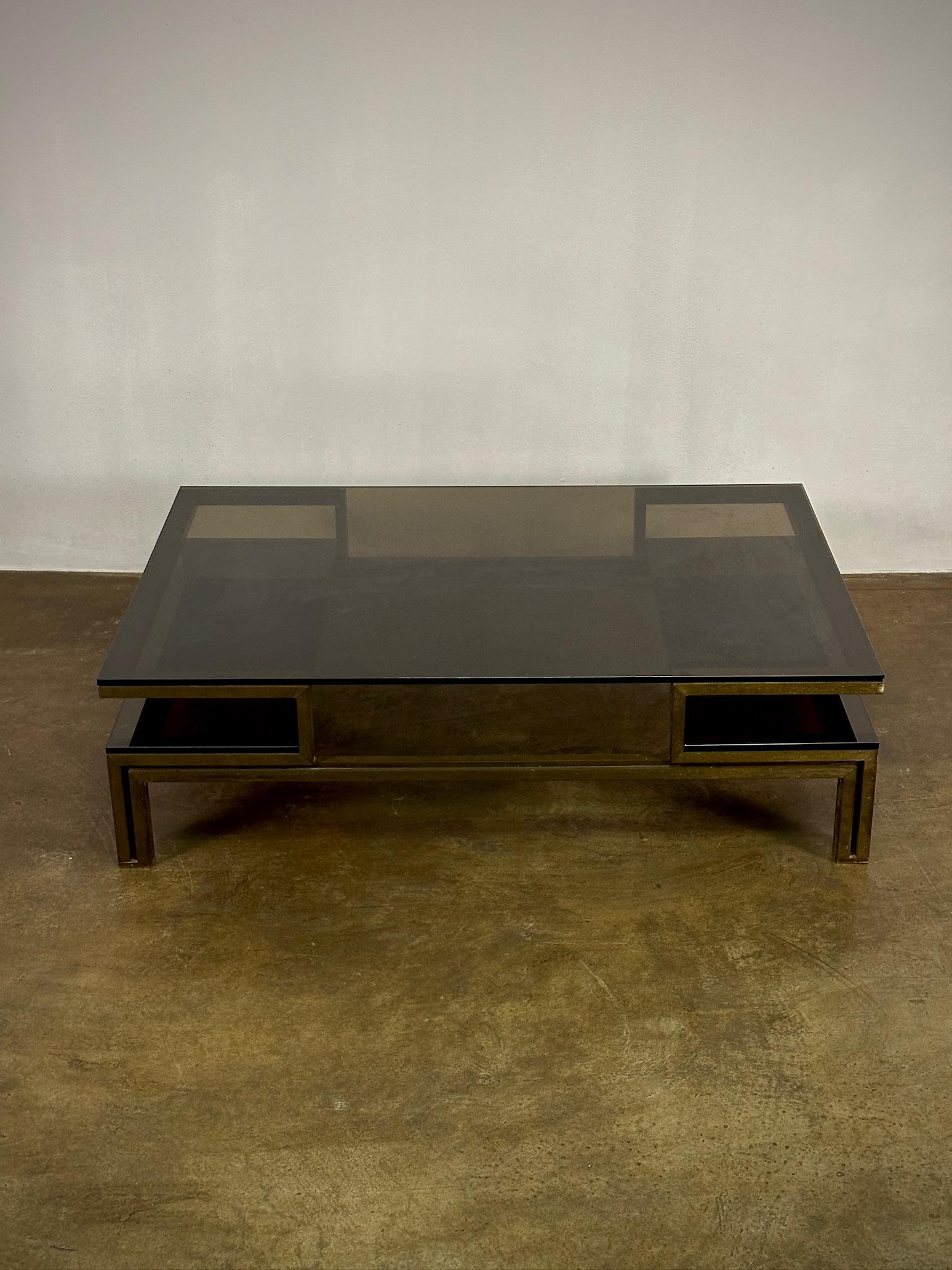 This Belgian mid-century coffee table merges function with the art of design, featuring a sleek glass top resting on a geometric brass base. The piece captures the essence of minimalist aesthetic with its clean lines and transparent surface,
