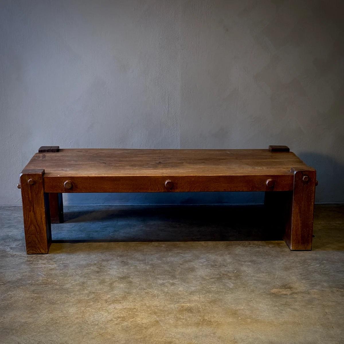 This solid oak coffee table exudes a rustic charm with its substantial construction and timeworn patina. Its sturdy, almost architectural build suggests a piece designed for both function and longevity. The visible grain, natural imperfections, and