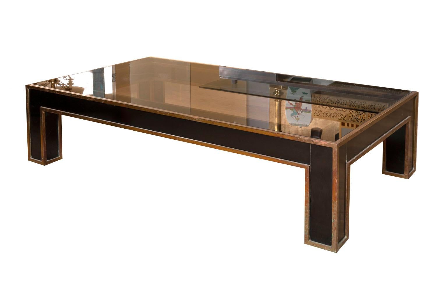 Rectangular coffee table in with thick square section legs with a background of black lacquer, crosspieces are similar. Gilt brass nets adorned angles edges of the whole structure. 
Smoked glass top, rectangular shaped.

Work from the 1970s.
 