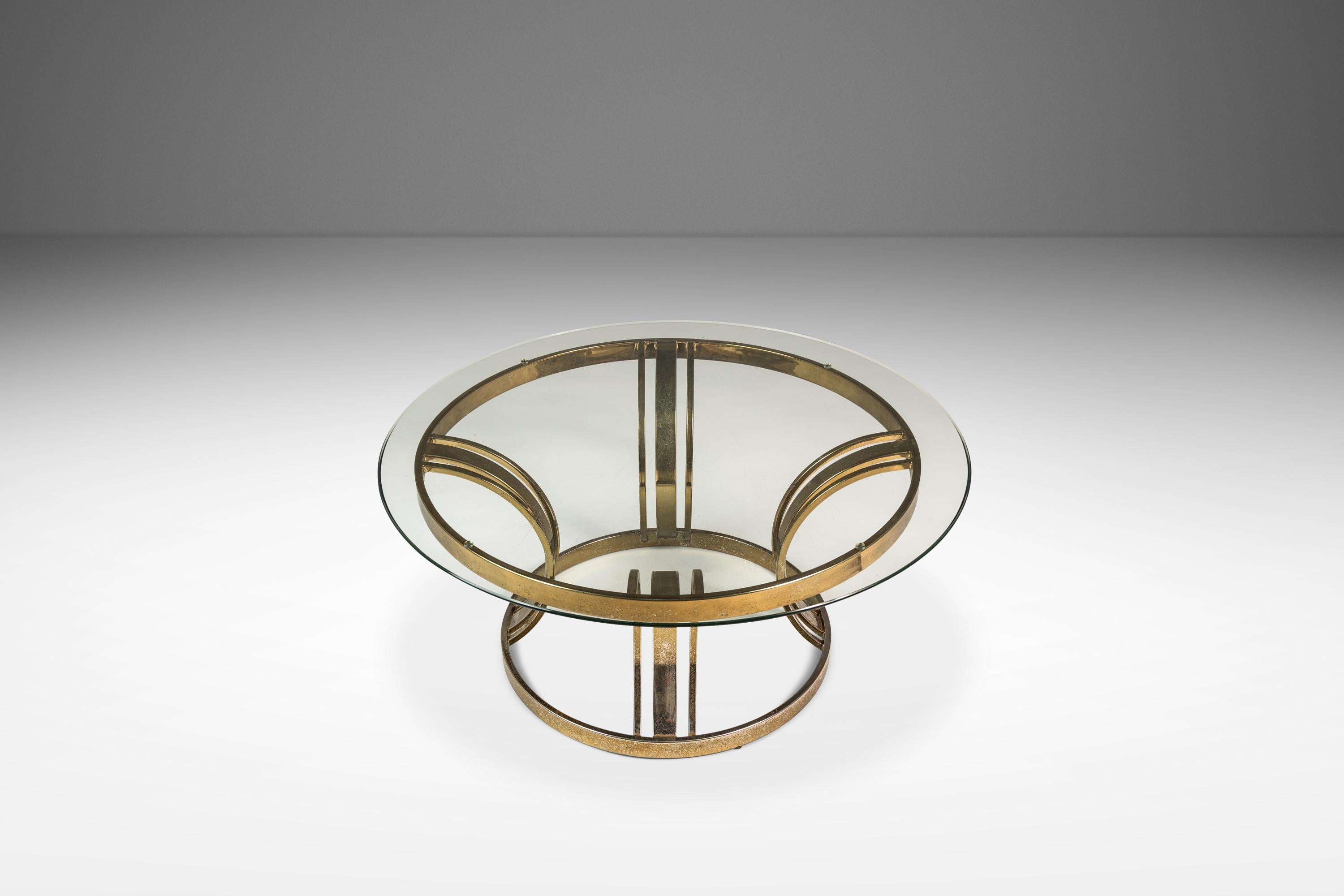 Voici une table basse ultra-stylée de style Régence hollywoodienne à la manière de Milo Baughman. Avec sa base polychrome plaquée laiton à la patine riche en caractère et son plateau en verre épais, cette table chic, avec sa position et son