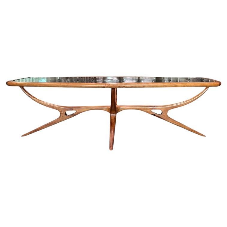 Esta mesa de centro tiene un armazón de madera dura de Caviuna y un tablero de cristal con cuatro patas. La mesa tiene forma ovalada y la madera presenta un bonito dibujo. La forma de la mesa y el estilo de las patas son lo que hace que esta pieza