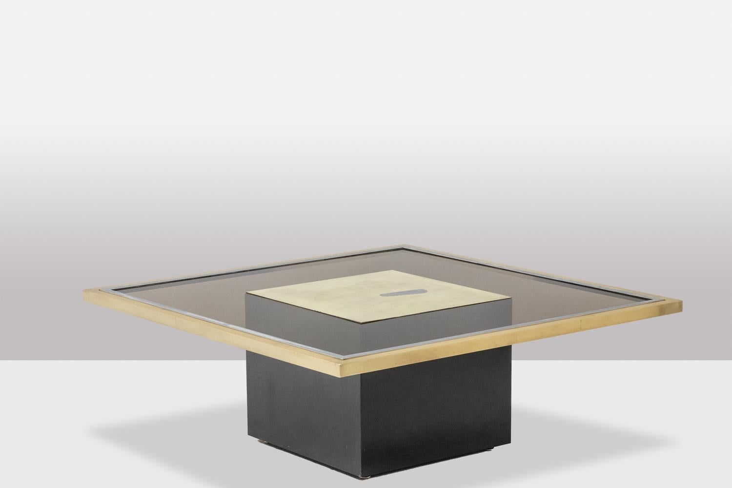 Table basse de forme carrée. Plateau en verre fumé présentant en son centre un carré décoratif en laiton doré et gravé composé de formes abstraites, dans son cadre en laiton doré et argenté et reposant sur une base carrée en bois laqué noir,