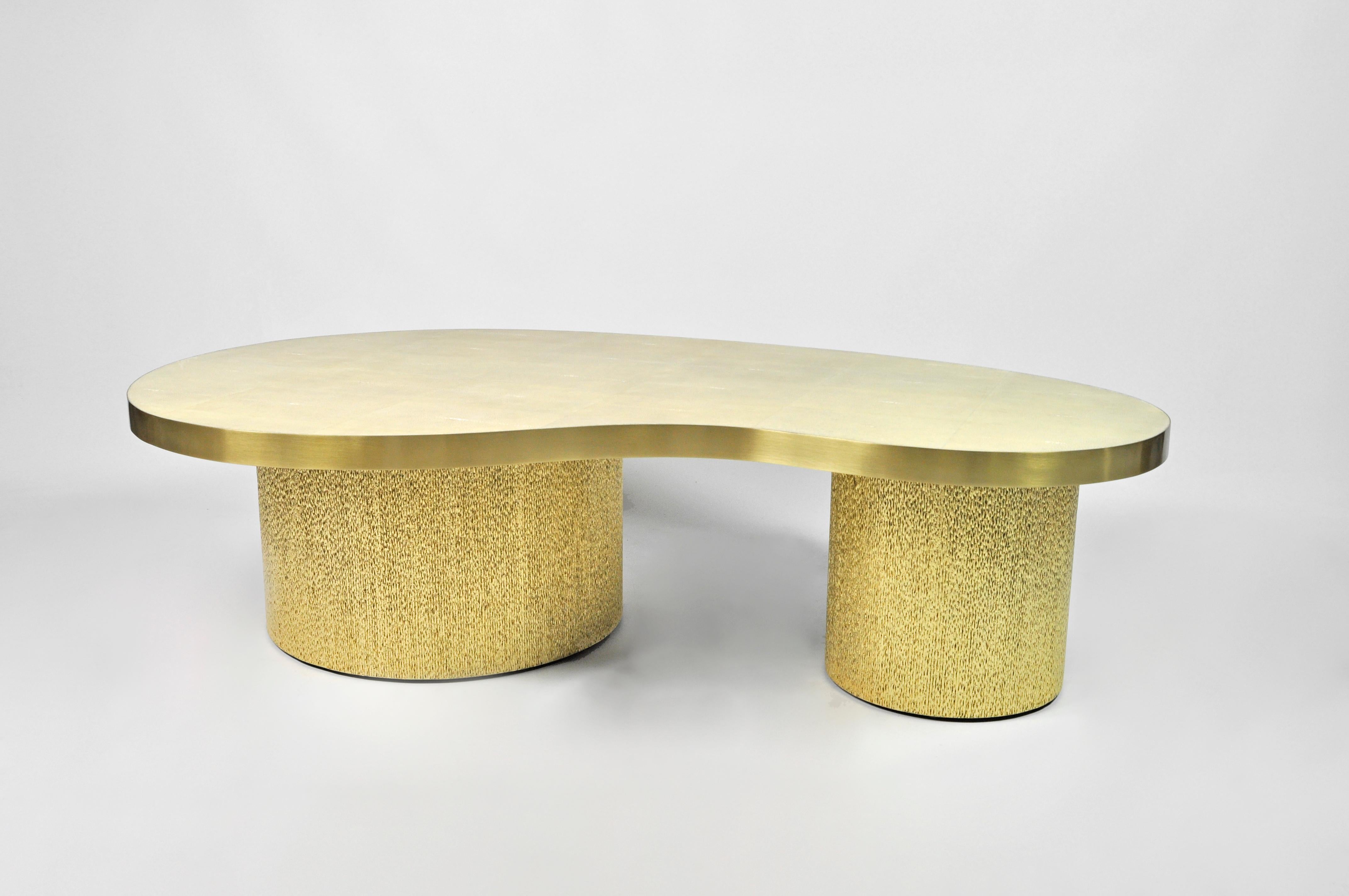 Cette table basse en forme de haricot est composée d'un plateau en galuchat avec des bords en laiton.
Il est monté sur des pieds cylindriques recouverts de marqueterie de fibres naturelles dorées .

Les dimensions de la table sont les suivantes