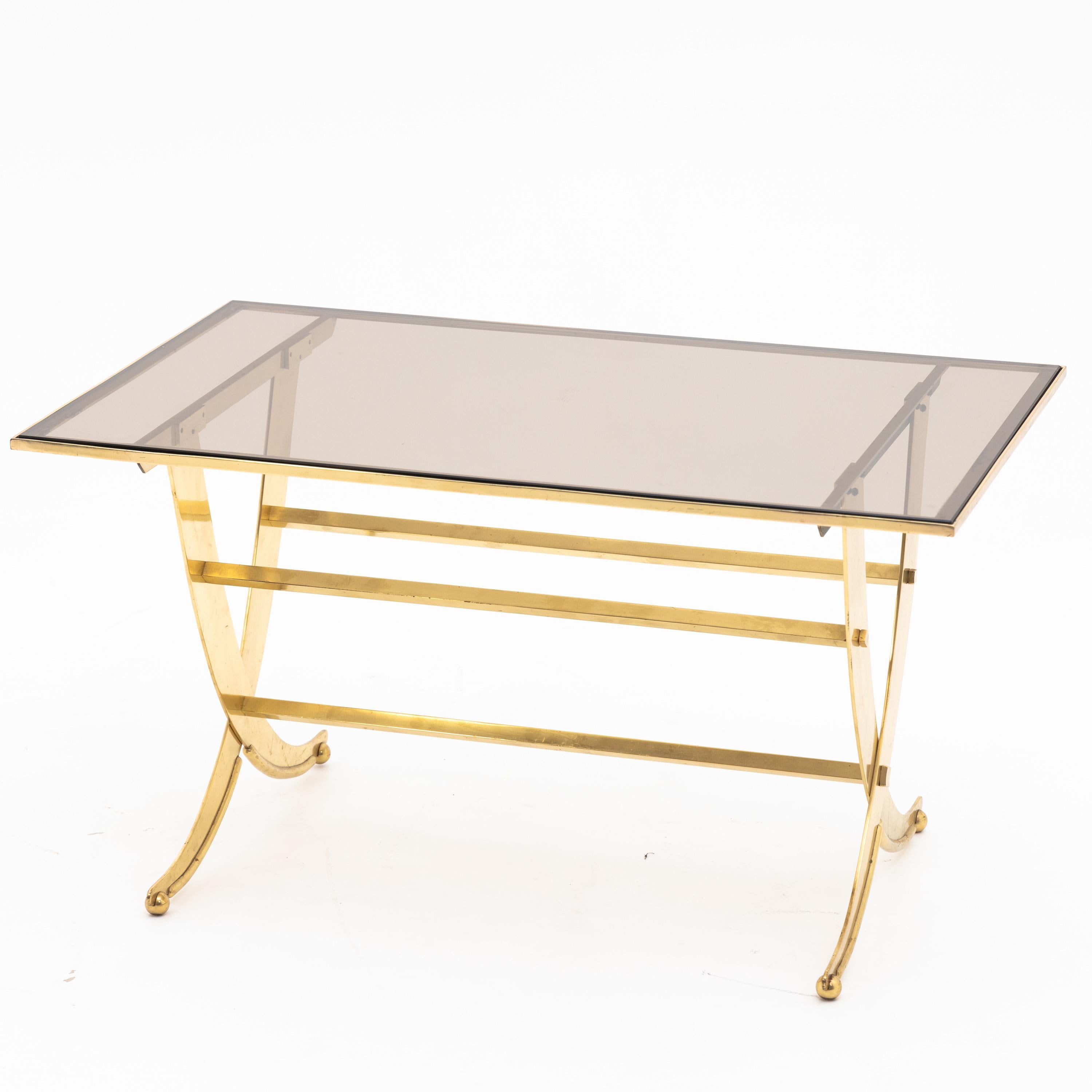 Coffee table standing on X-shaped brass frame with rectangular smoked glass top.