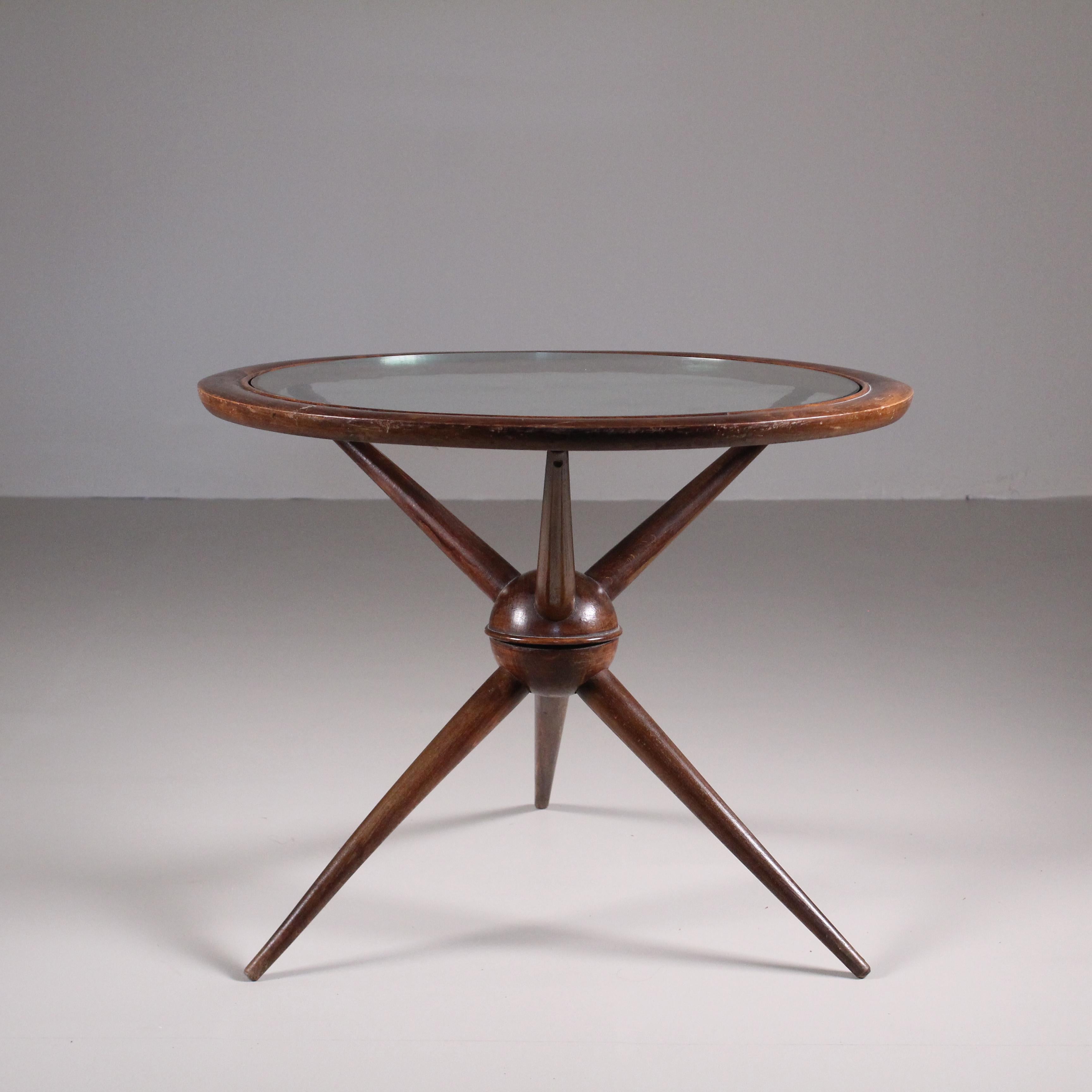 This charming Mid-Century style round coffee table is an elegant fusion of wood and glass. Its base, made of fine wood, flaunts woven legs with sinuous, slender lines typical of the iconic mid-century style. The table top is a thin, transparent