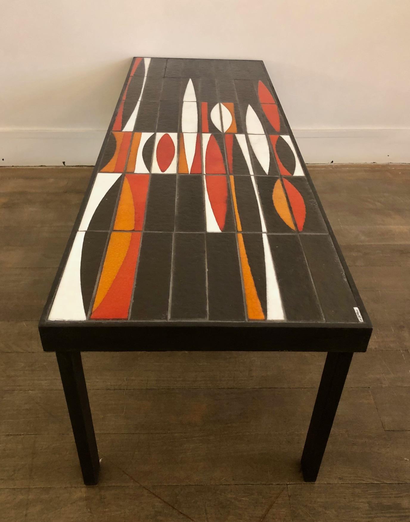 Coffee table composed of a partially glazed ceramic top and a black lacquered metal base. 
Ceramic tiles with white, red and orange « Navette » decoration. 
Model 