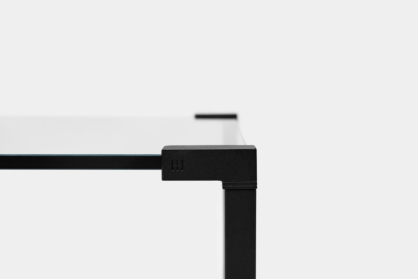 This minimalistic table by GHYCZY consists of a glass tabletop with black stainless-steel legs. The legs of the iconic table are made of tubes and casted parts which clamp the glass. On the casted parts the minimalistic GHYCZY logo is visible. The