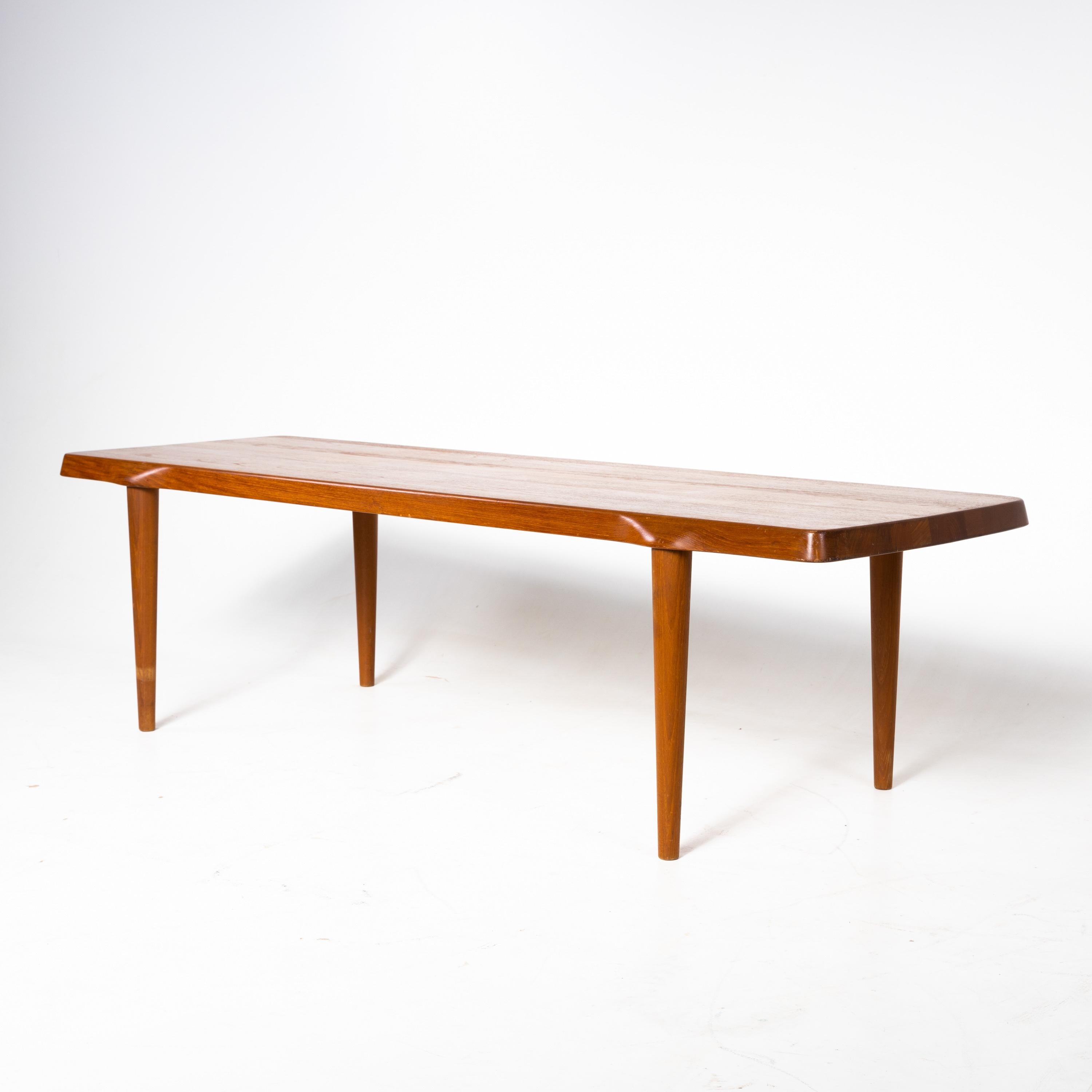 Midcentury design coffee table standing on four conical legs. The transition between the legs and the tabletop is slightly wavy and the edge of the table top is slightly angled. Signs of age and wear in the form of slight scratches.